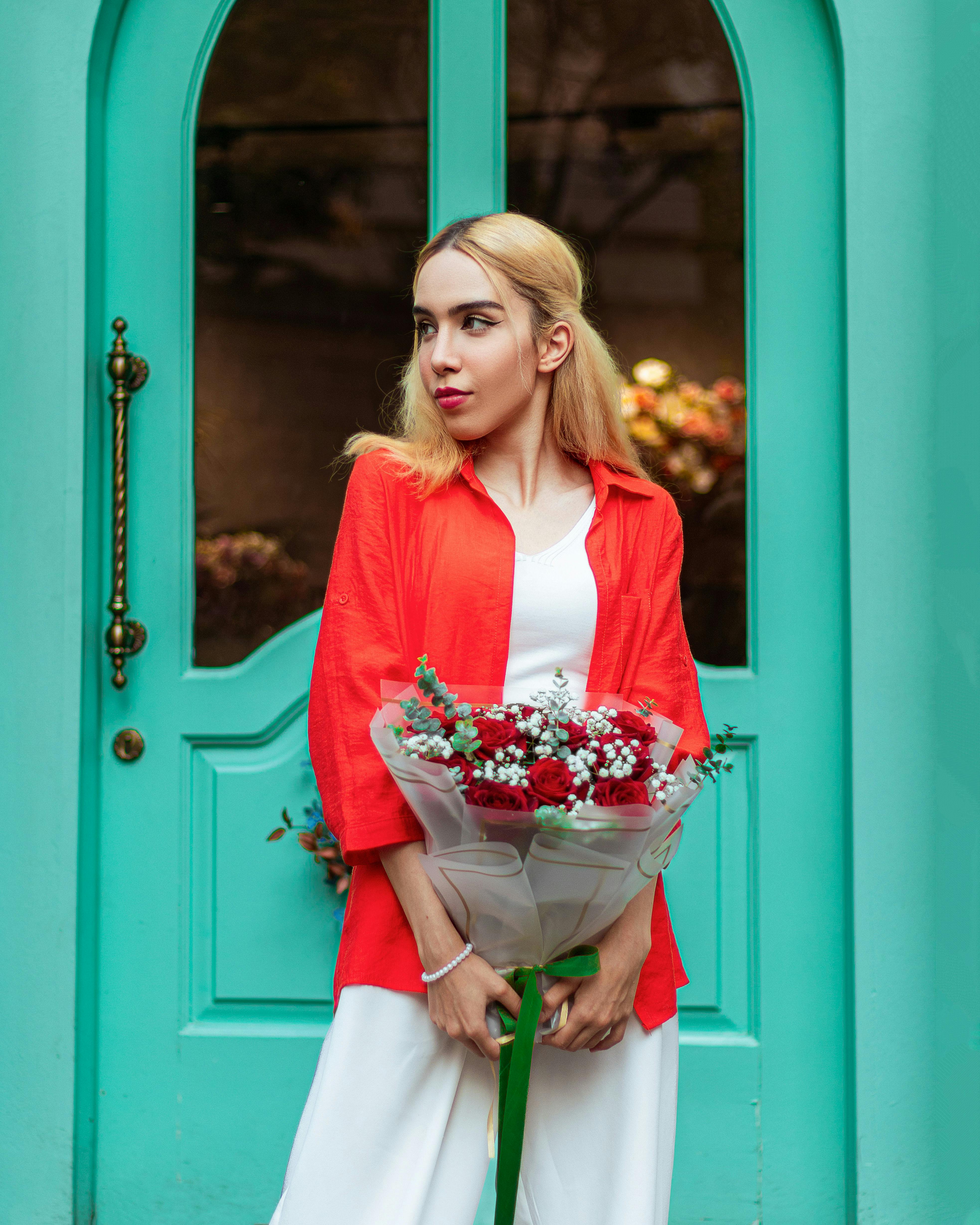 Gratis Una giovane donna è in piedi con un bouquet davanti a una porta color turchese acceso, emanando un senso di freschezza e colore. Foto a disposizione
