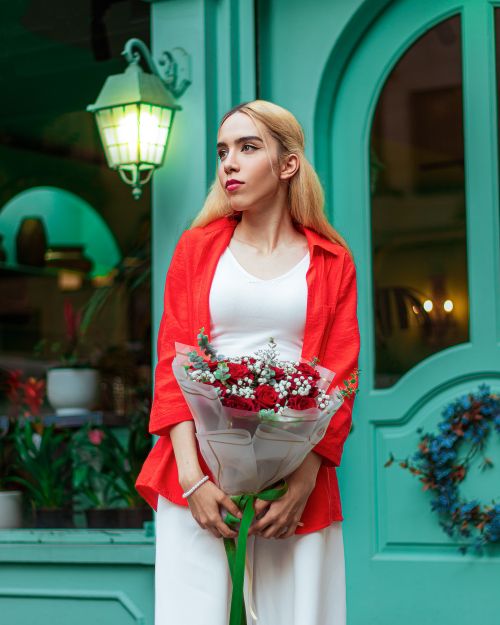 Free Stylish woman in red shirt holding a floral bouquet in front of a turquoise door. Stock Photo