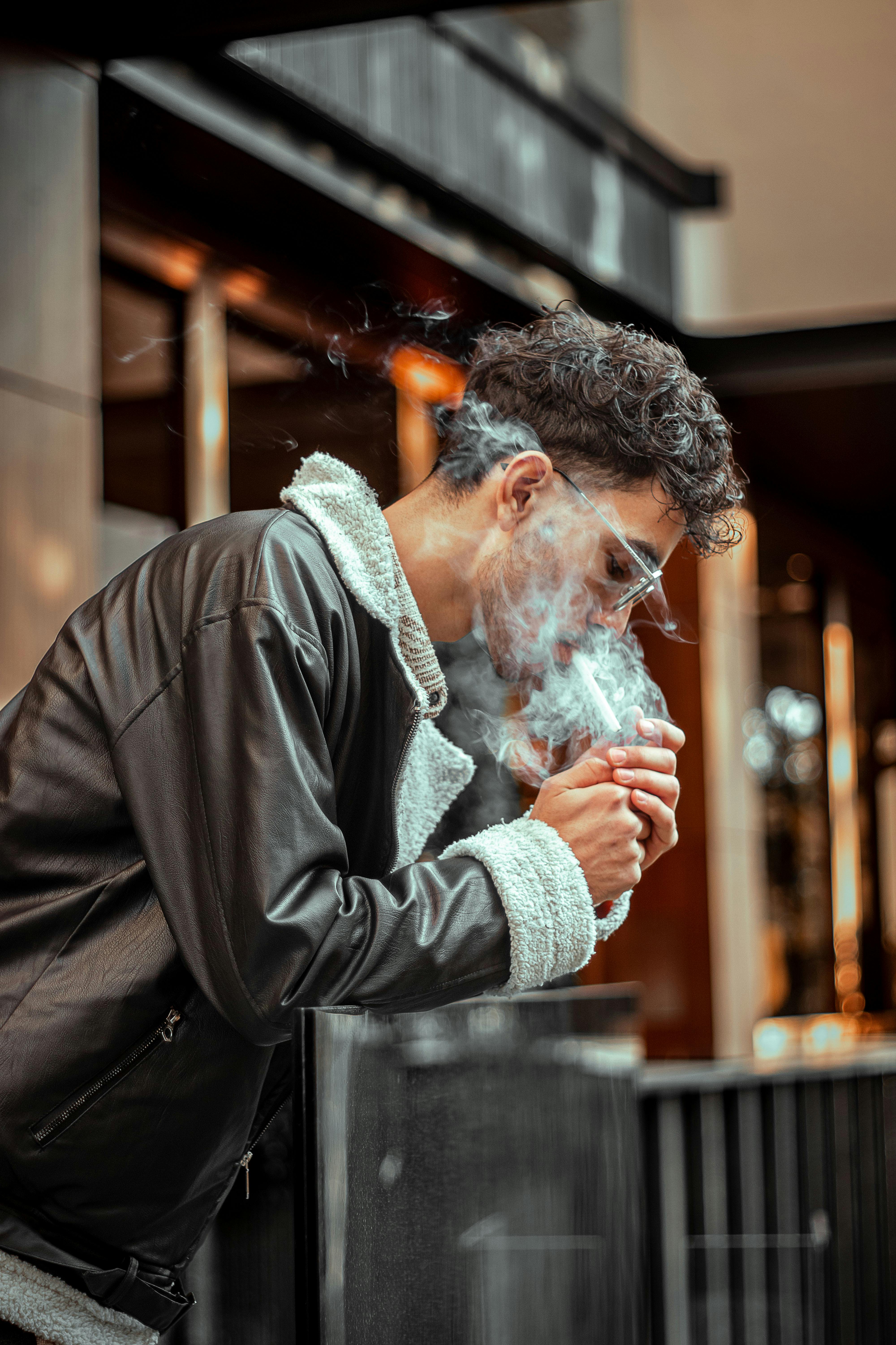 Miễn phí Hình ảnh cận cảnh một thanh niên đang nhả khói thuốc ngoài trời trong khung cảnh thành phố. Ảnh lưu trữ