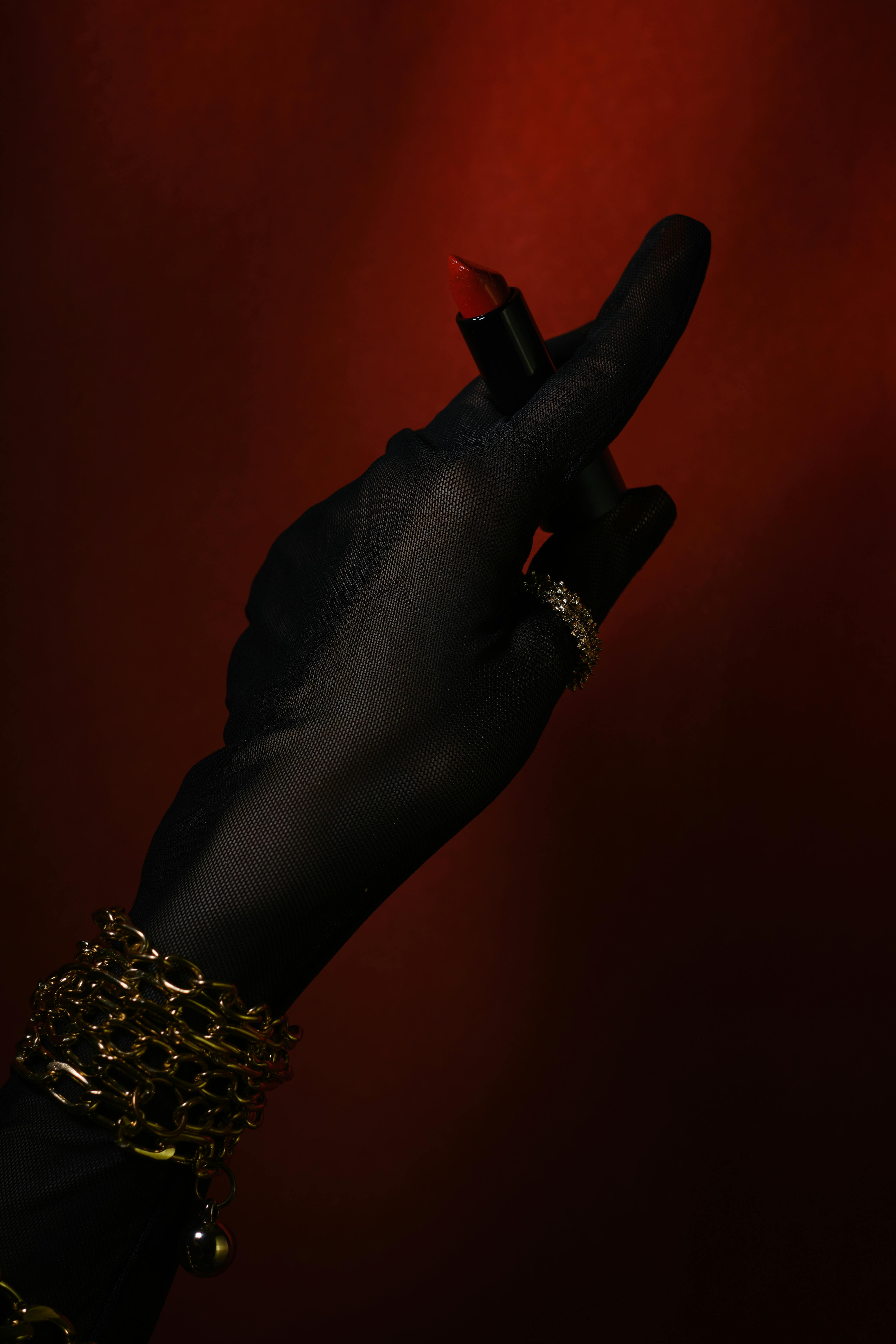 Ücretsiz Şık, siyah eldivenli bir el, koyu kırmızı bir arka plan üzerinde lüks bir kırmızı ruj sergiliyor. Stok Fotoğraflar