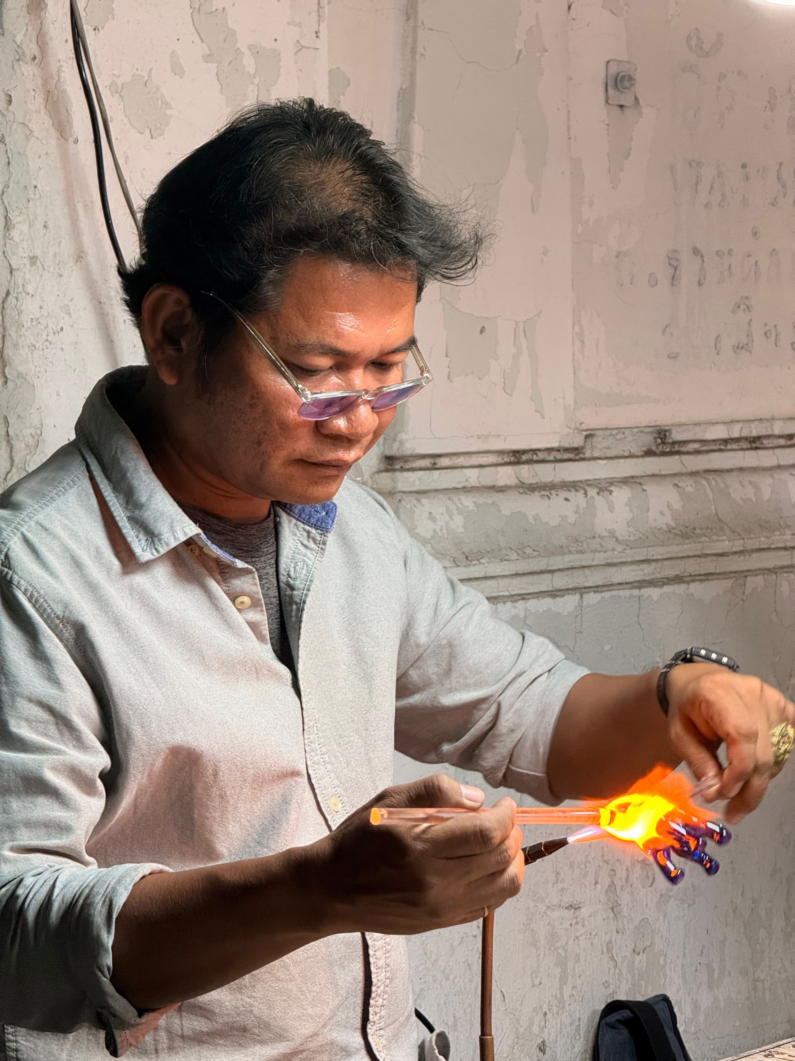 Skilled artisan shaping glass sculpture using flame in a workshop setting. Focused craftsmanship and technique.