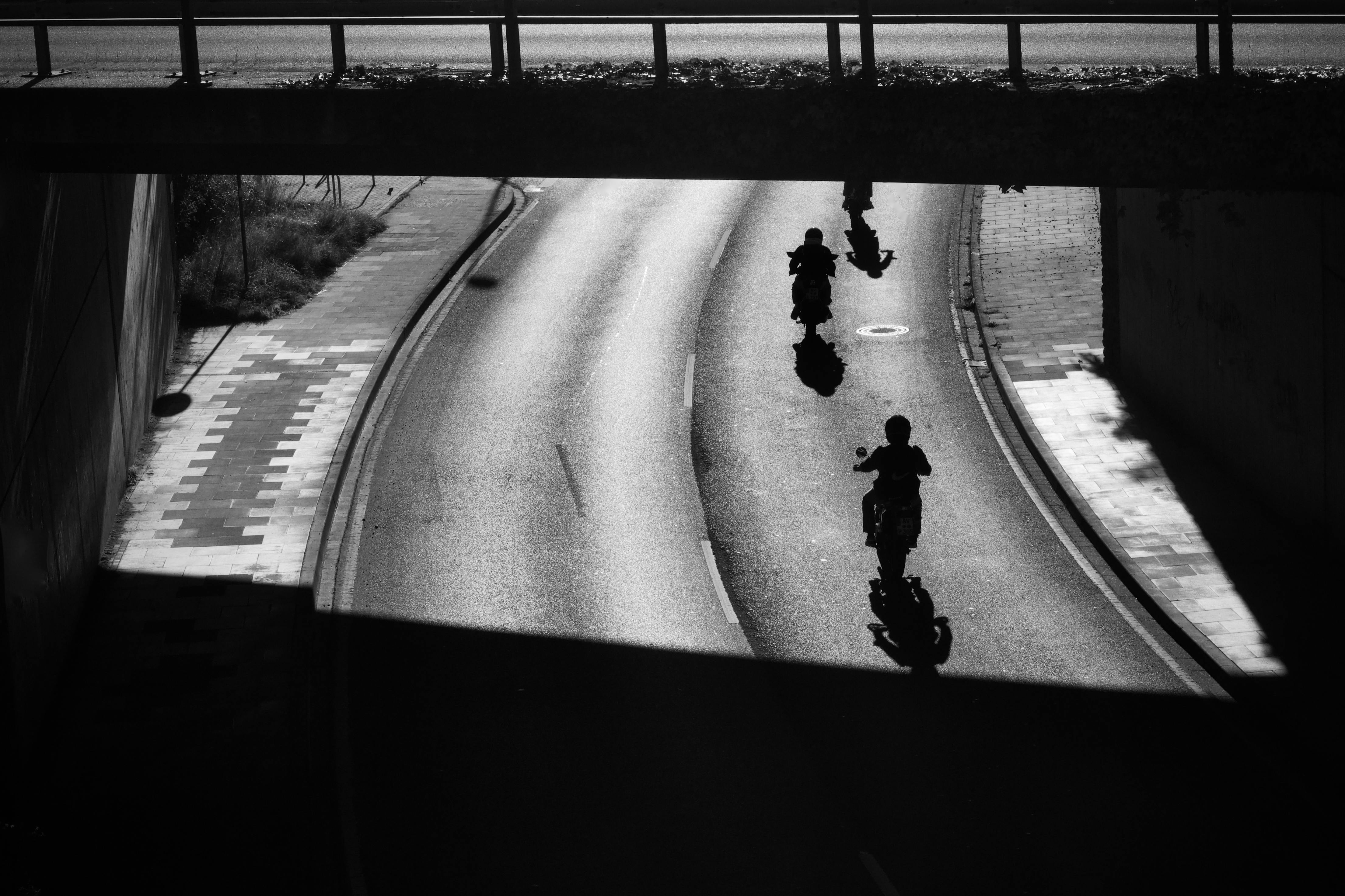 bezplatná Siluety motorkářů jedoucích pod mostem v dramatickém černobílém kontrastu. Základová fotografie