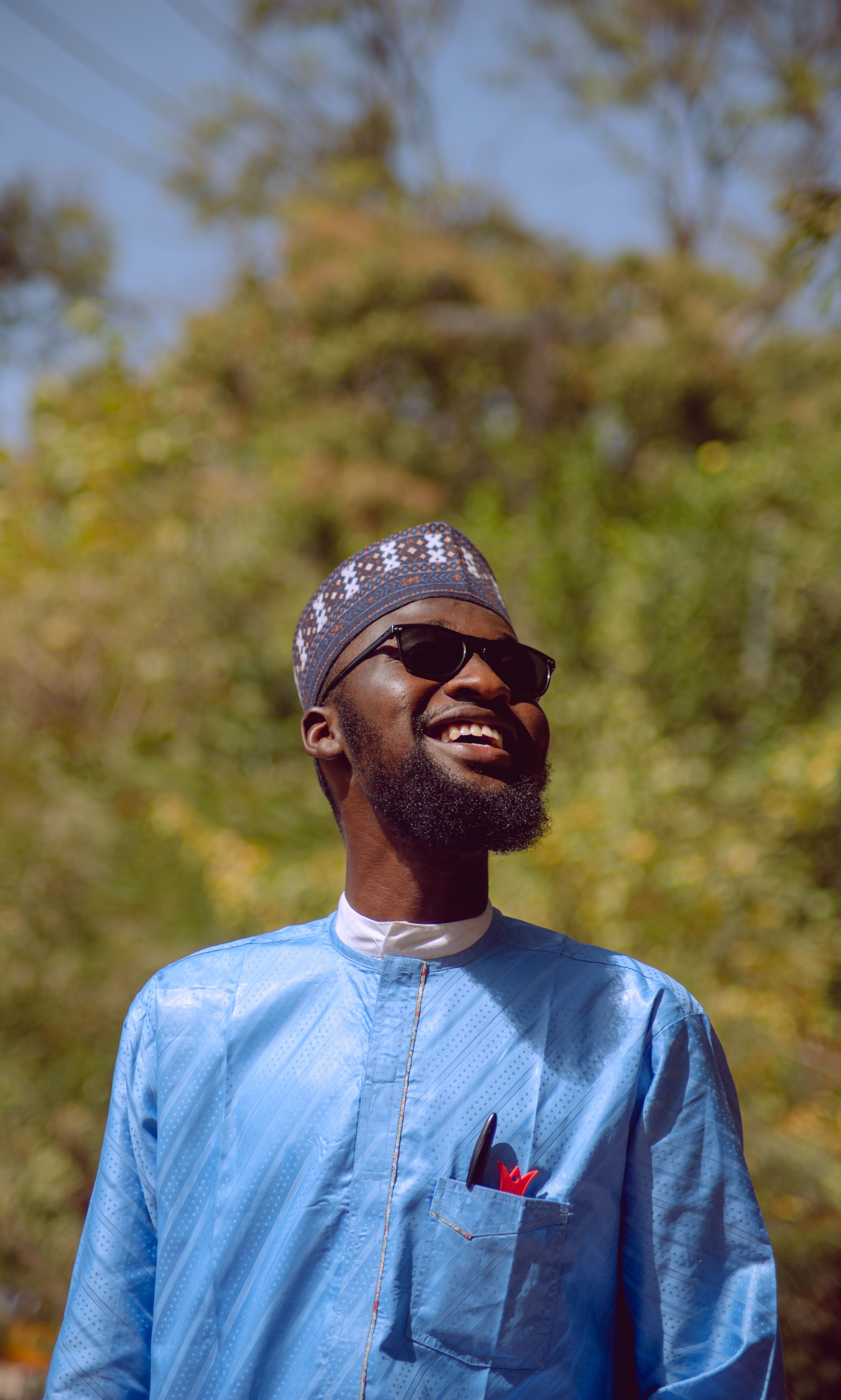 A cheerful man in sunglasses wearing traditional Nigerian attire, outdoors in Zaria, Nigeria.