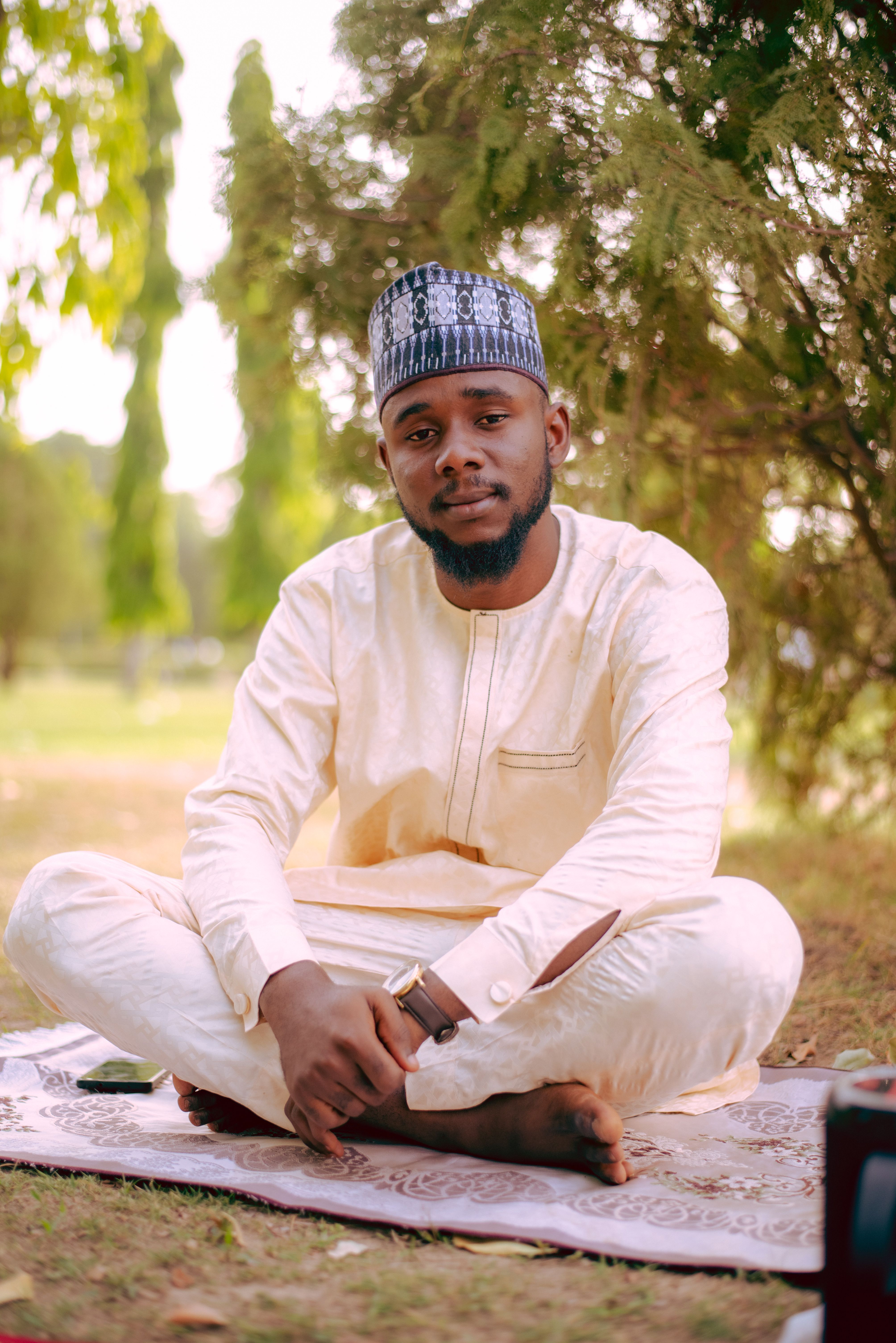 A young man sitting outdoors in traditional Nigerian attire, exuding calmness and cultural pride.