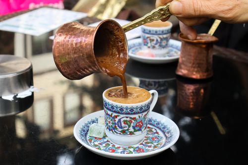 Free A hand pours Turkish coffee from a copper cezve into a decorative cup. Outdoor ambiance. Stock Photo