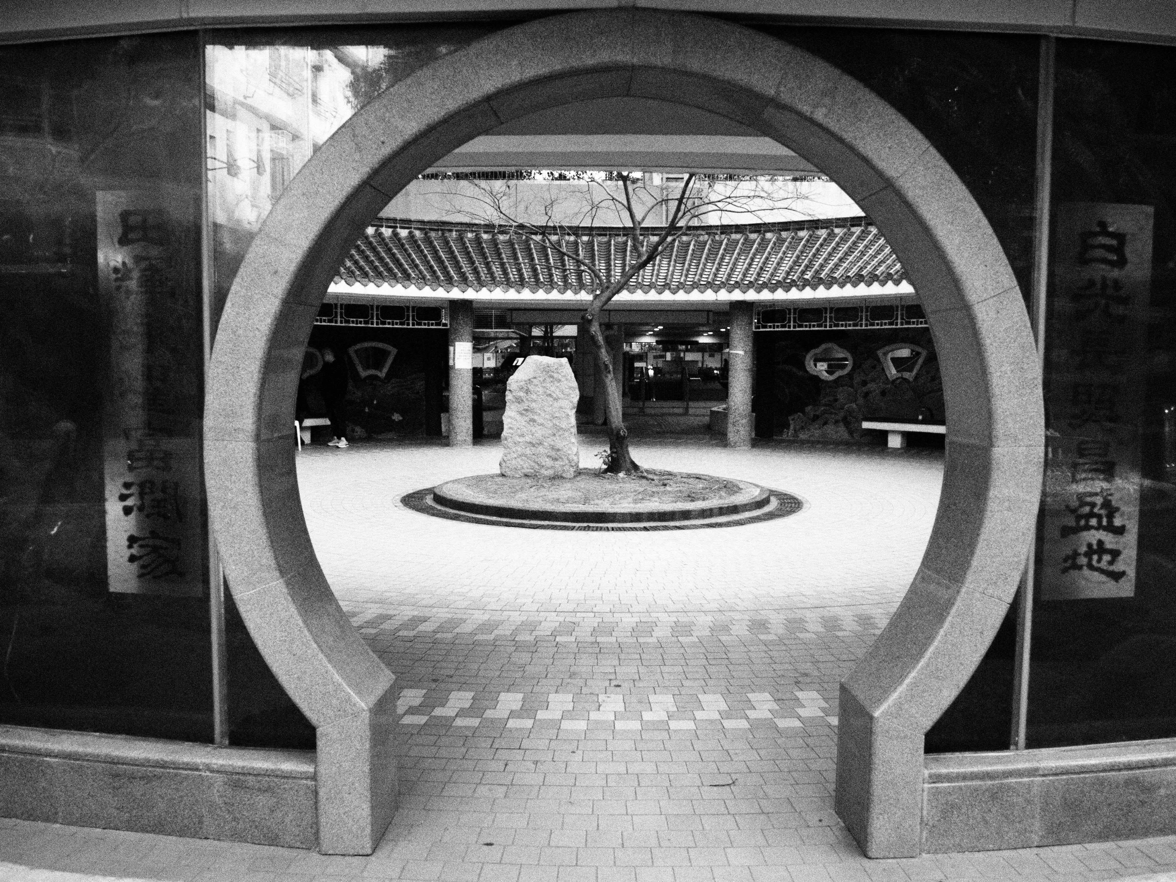 Gratis Foto in bianco e nero di un cortile tradizionale visto attraverso un cancello rotondo a forma di luna a Hong Kong. Foto a disposizione