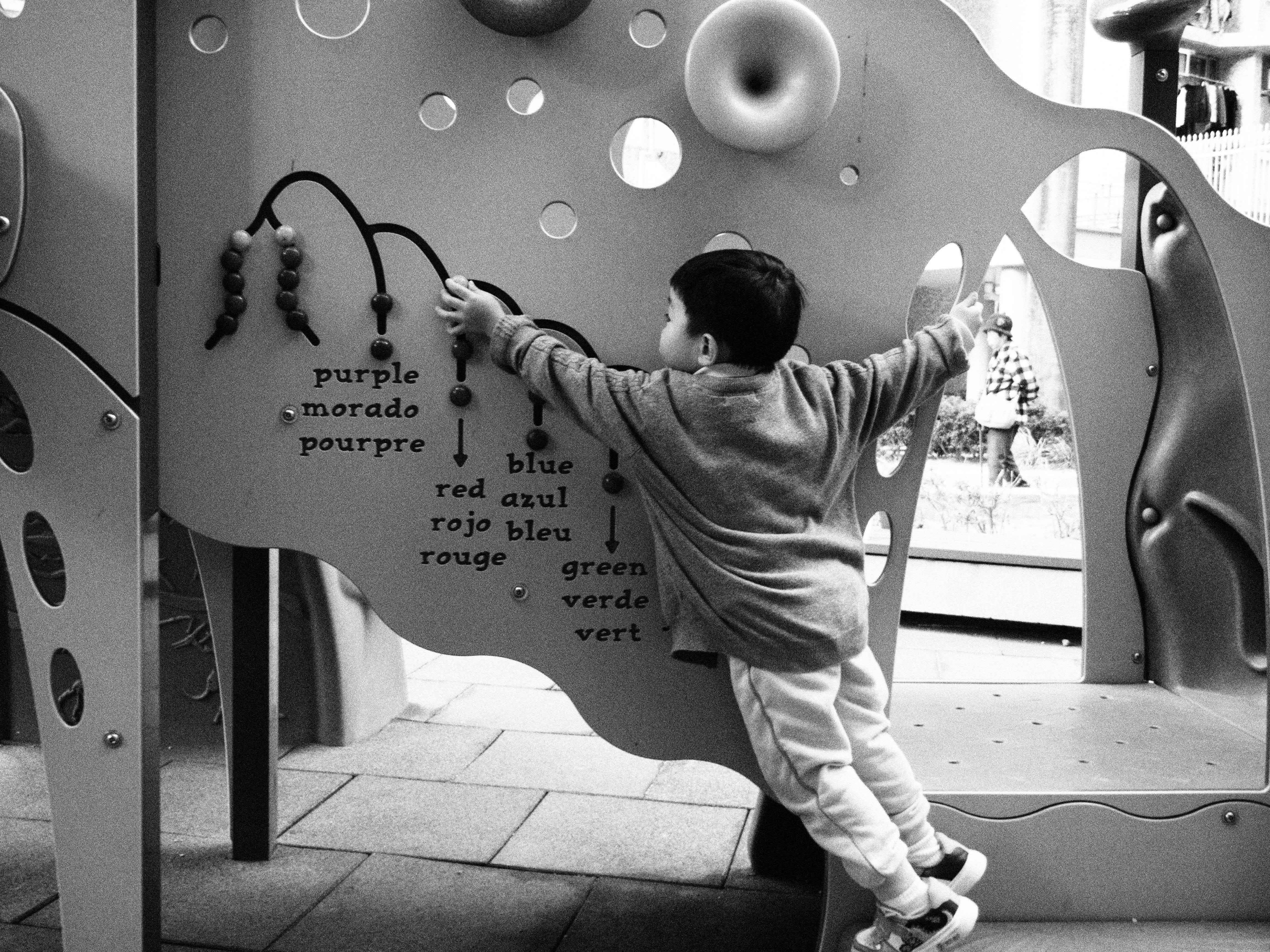 A young child interacts with a colorful educational play wall in a Hong Kong playground.