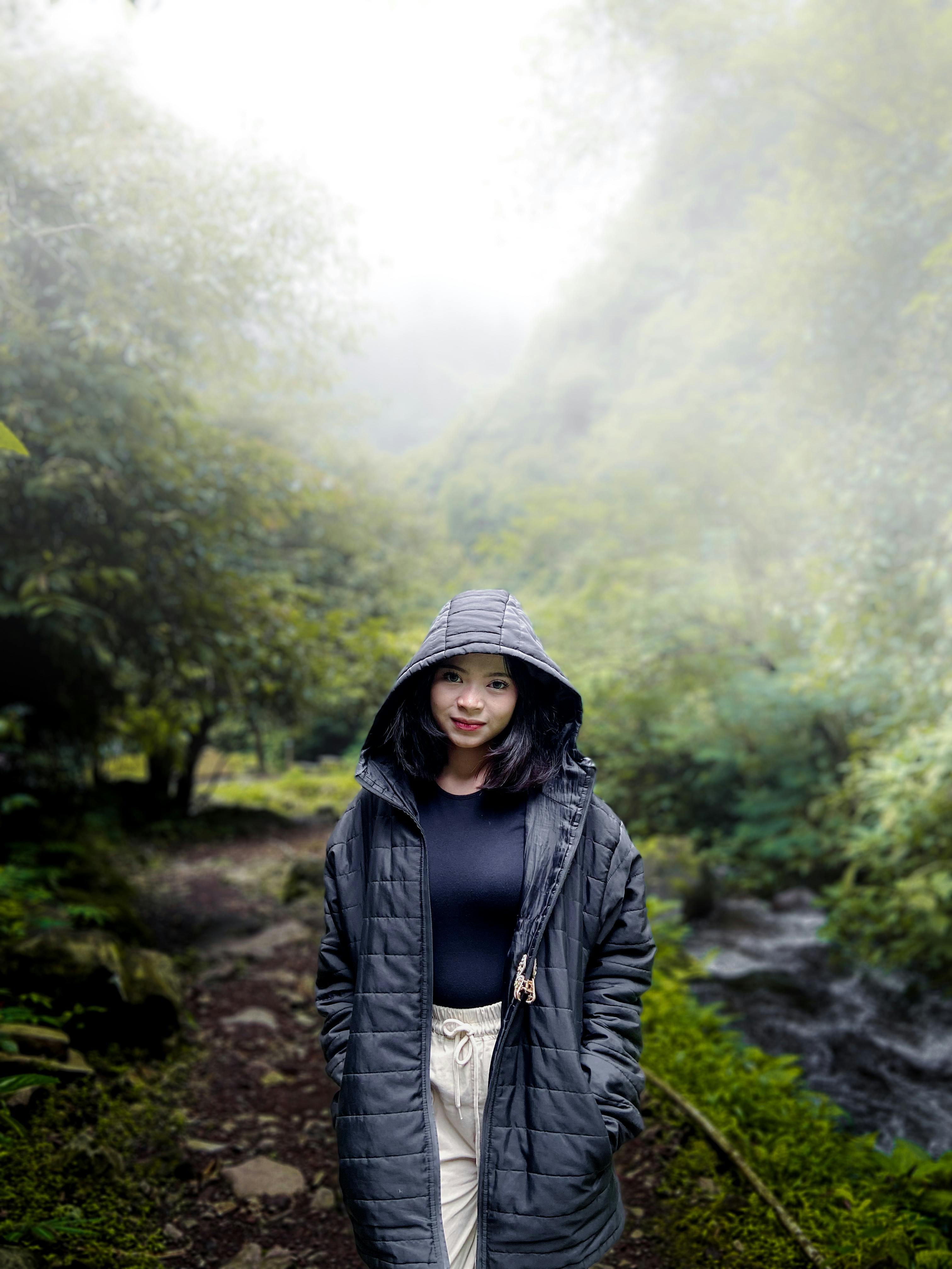 Gratis Giovane donna in una foresta nella Giava Occidentale, Indonesia, che indossa un cappotto con cappuccio in una giornata nebbiosa. Foto a disposizione