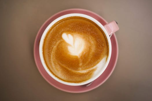 Aerial shot of latte with beautiful leaf art in a pink cup on a saucer.
