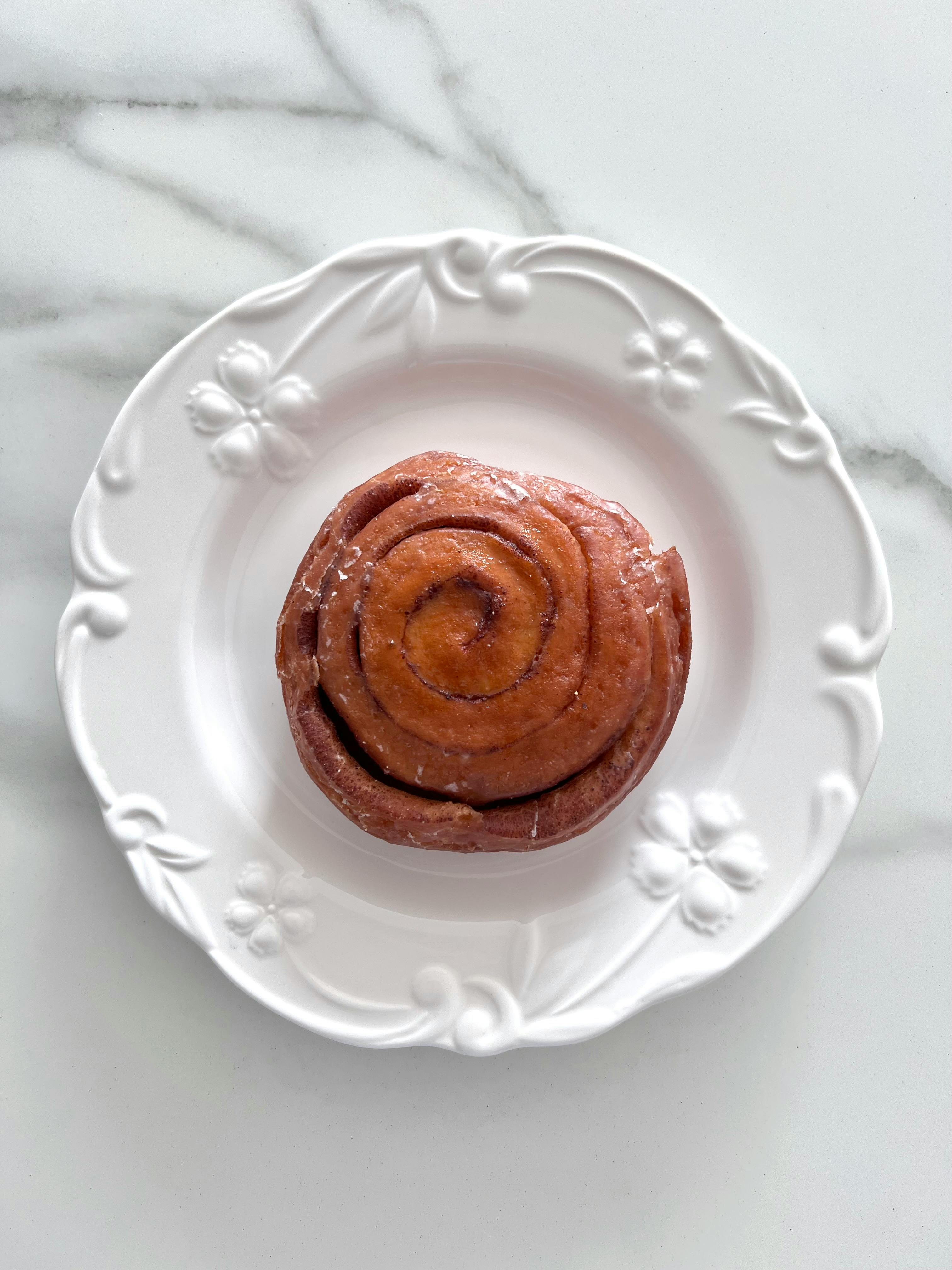 Kostenlos Frisch gebackene Zimtschnecke auf einem verzierten Keramikteller, perfekt zum Frühstück. Stock-Foto