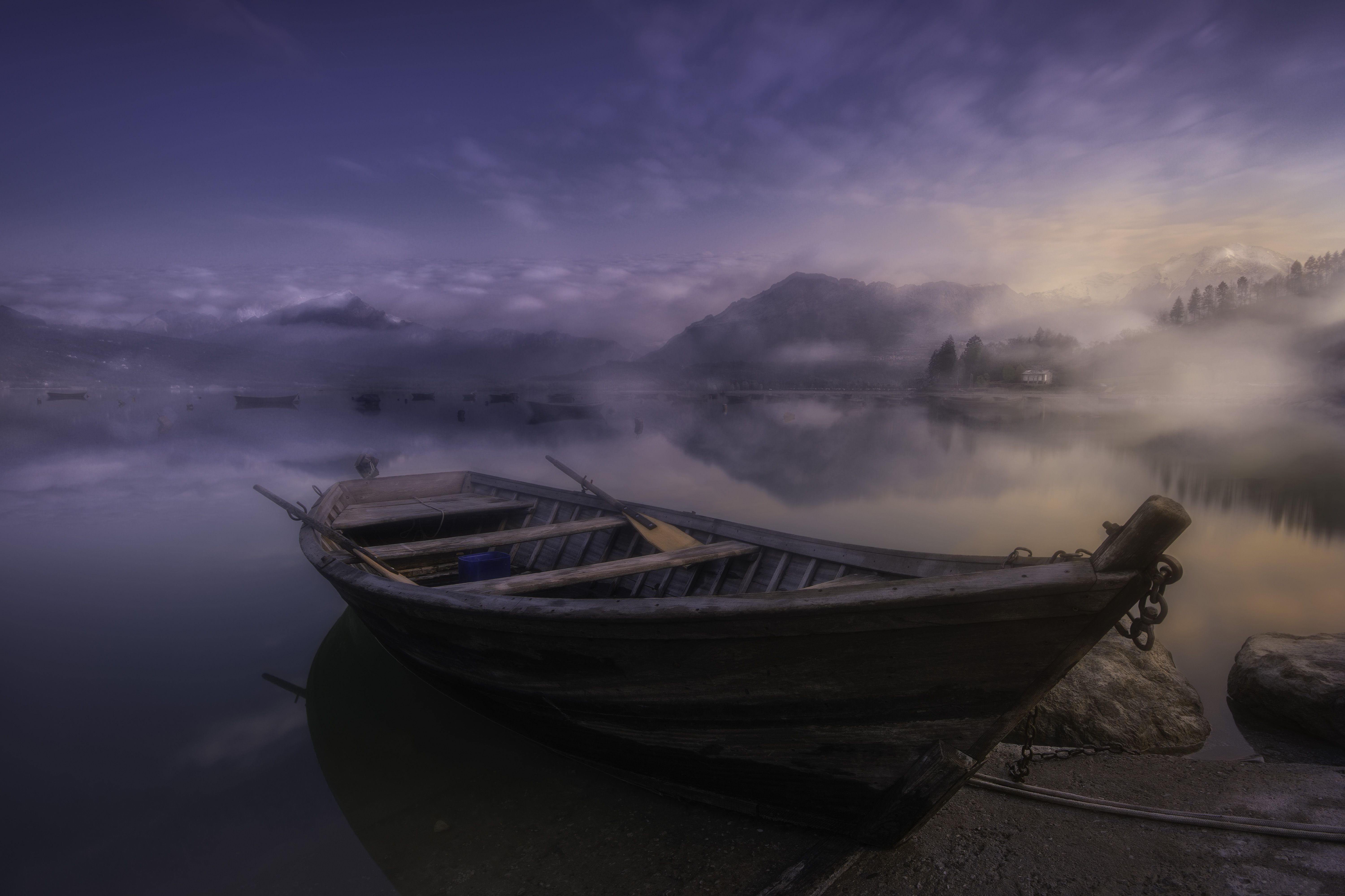Serene scene of a wooden boat in the misty waters at dawn with mountain reflections in Santa Croce, Veneto, Italy.