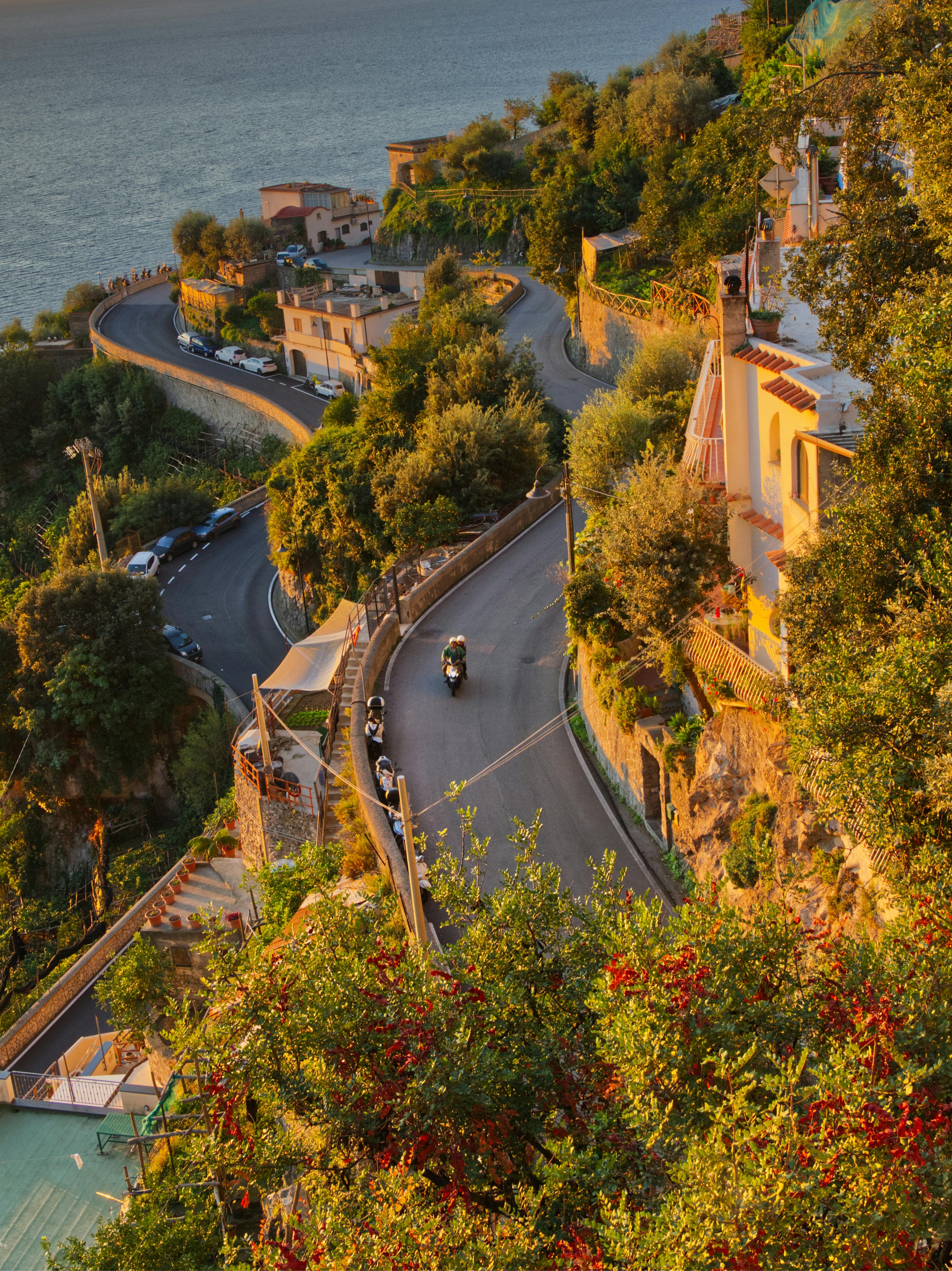 Miễn phí Một khung cảnh tuyệt đẹp nhìn từ trên cao xuống con đường ven biển quanh co với cây cối xanh tươi và sắc hoàng hôn rực rỡ. Ảnh lưu trữ