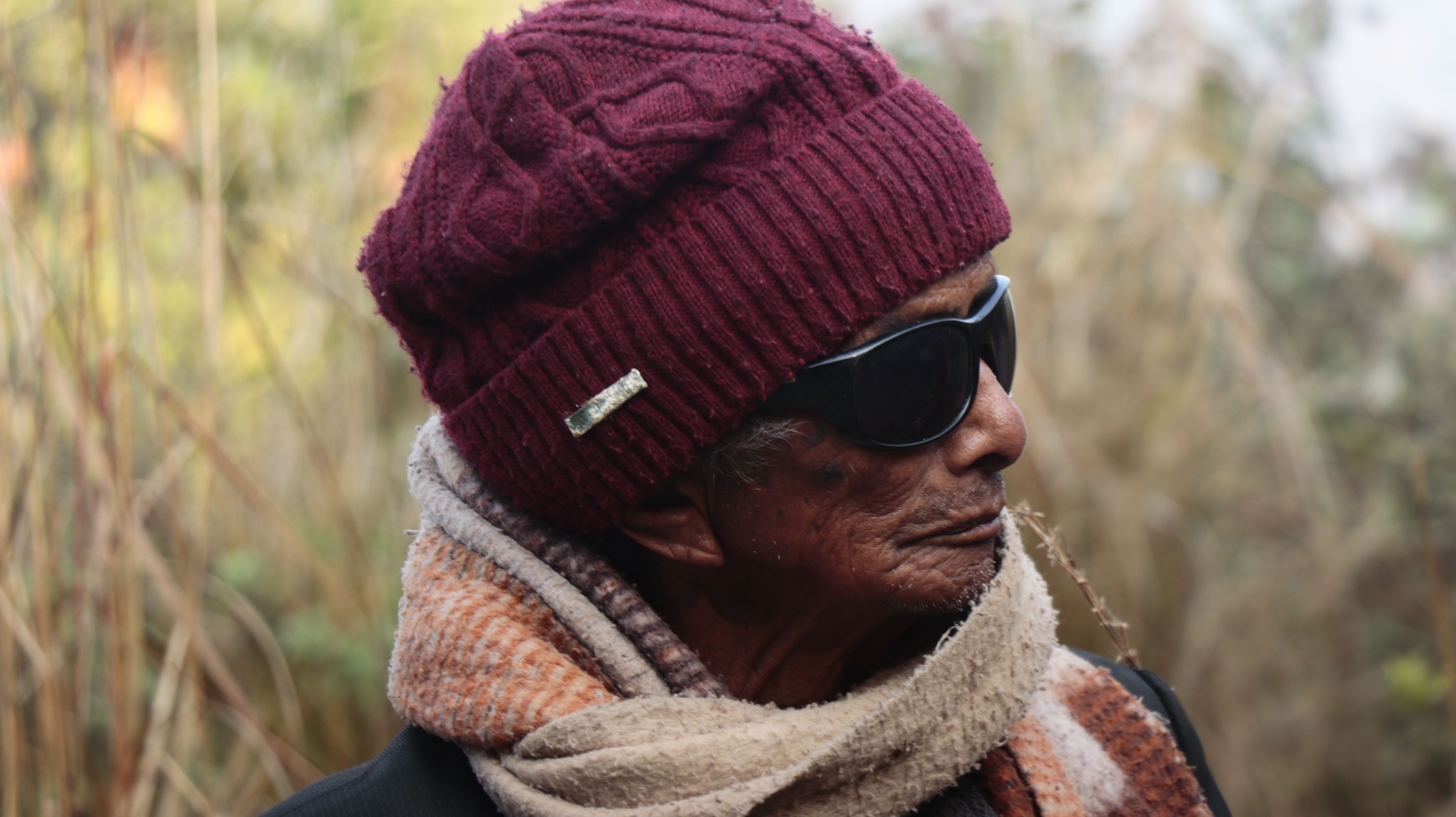Close-up of a senior adult wearing warm clothes and sunglasses outdoors.