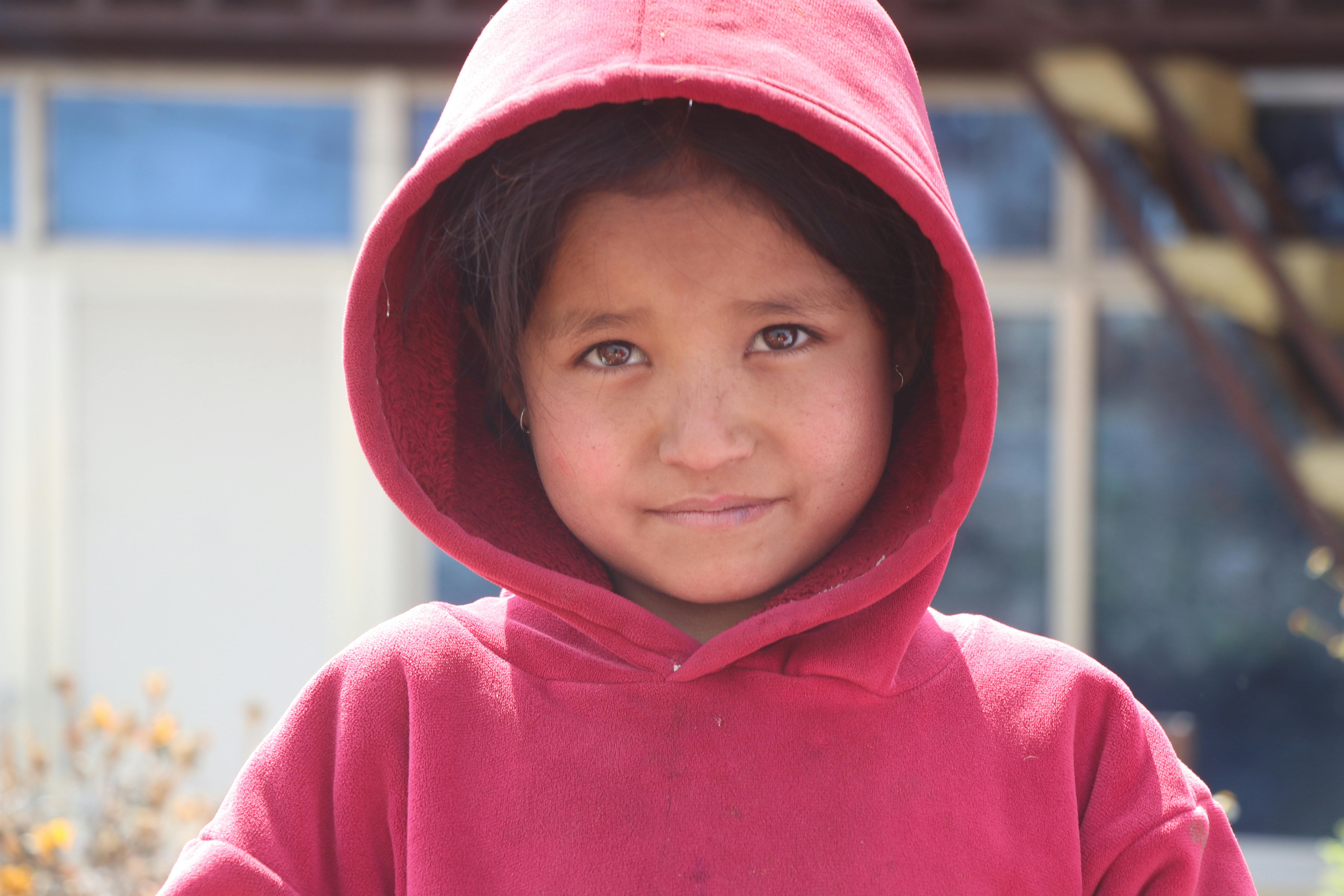 ingyenes Fiatal lány piros kapucnis pulóverben néz a kamerába a szabadban, napfényben. Stockfotó