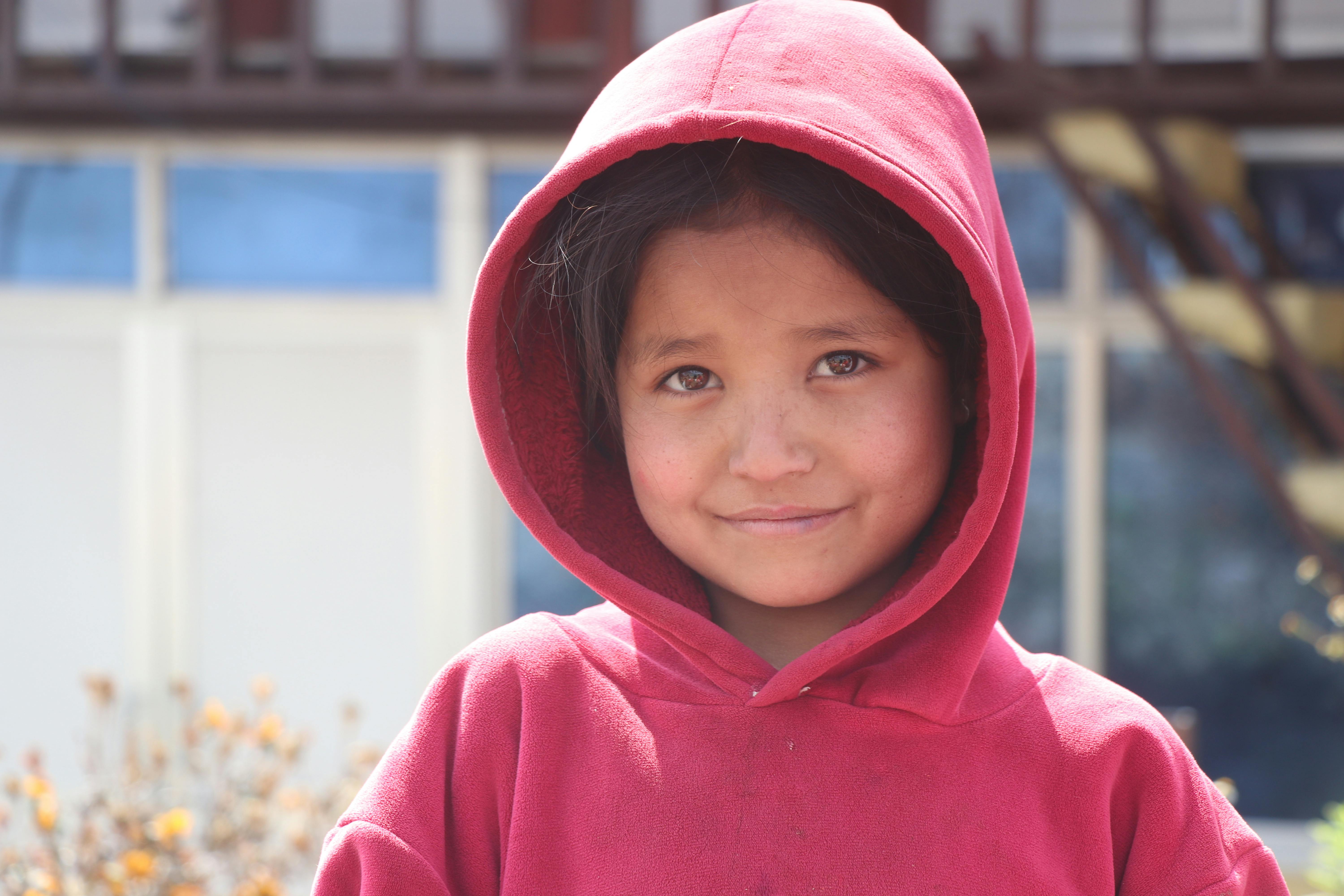 Δωρεάν Ένα νεαρό κορίτσι με κόκκινο φούτερ χαμογελάει θερμά ενώ στέκεται έξω. Φωτογραφία από στοκ φωτογραφιών