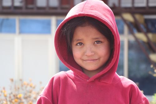Free A young girl with a red hoodie smiling warmly while standing outdoors. Stock Photo
