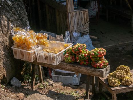 A rustic outdoor market stall showcasing fresh produce in bags and baskets under sunlight.