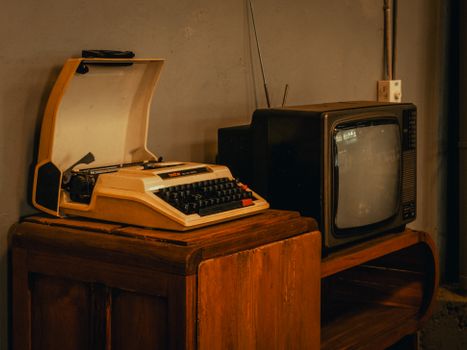 A nostalgic scene featuring a classic typewriter and an old-style TV on a rustic wooden table, indoors.