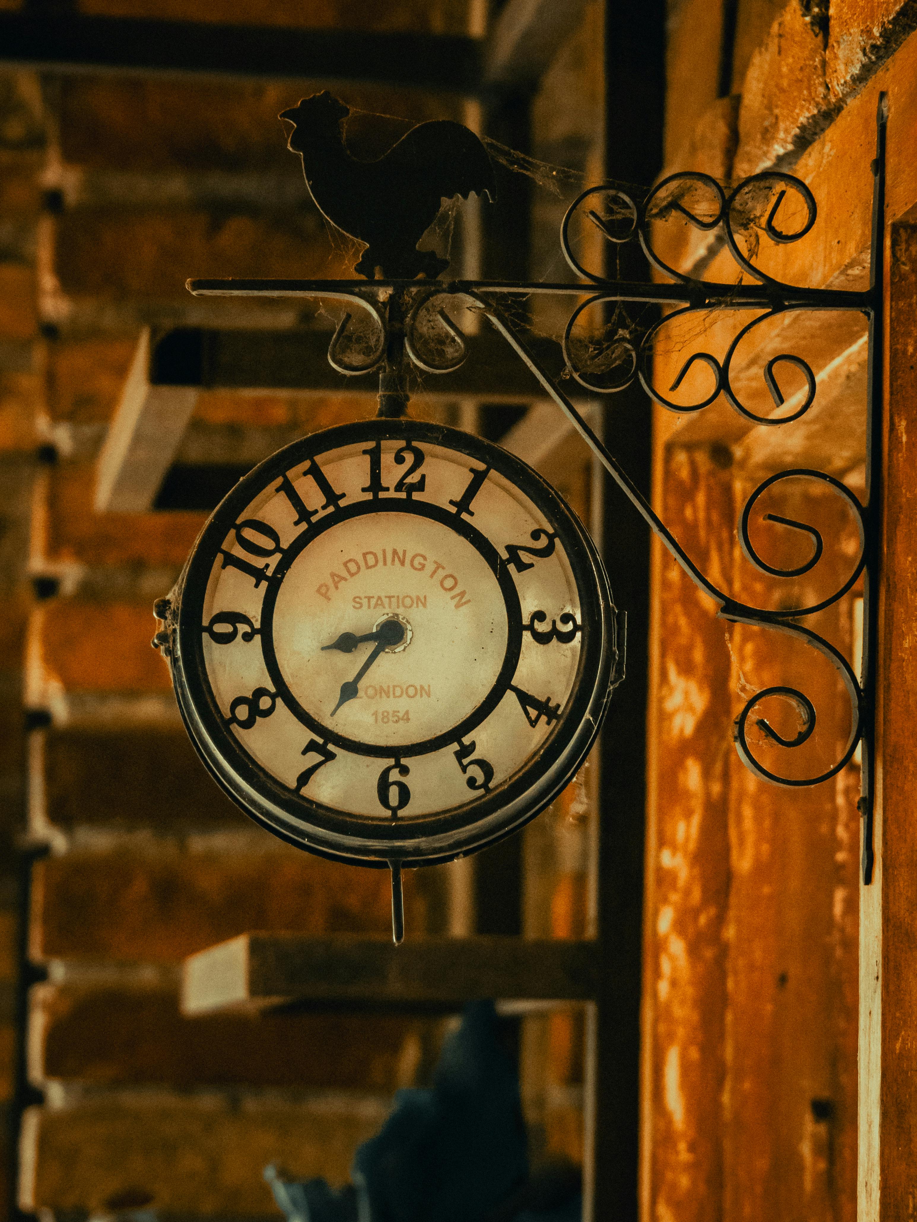 Free Rustic wall-mounted clock with a rooster design, featuring Paddington Station text, captured indoors with warm lighting. Stock Photo