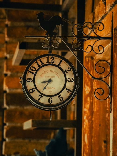 Free Rustic wall-mounted clock with a rooster design, featuring Paddington Station text, captured indoors with warm lighting. Stock Photo
