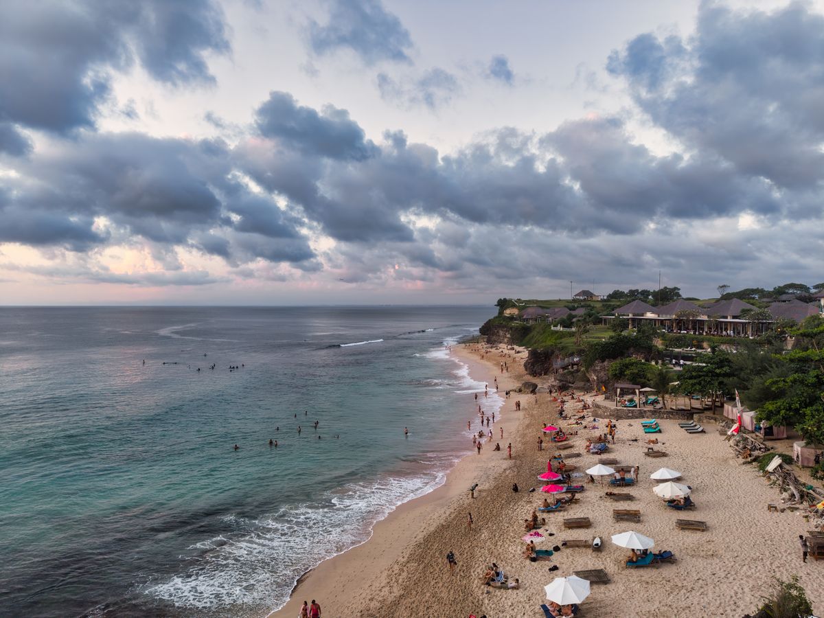Stunning aerial view of a beach in Bali, Indonesia with visitors at sunset.