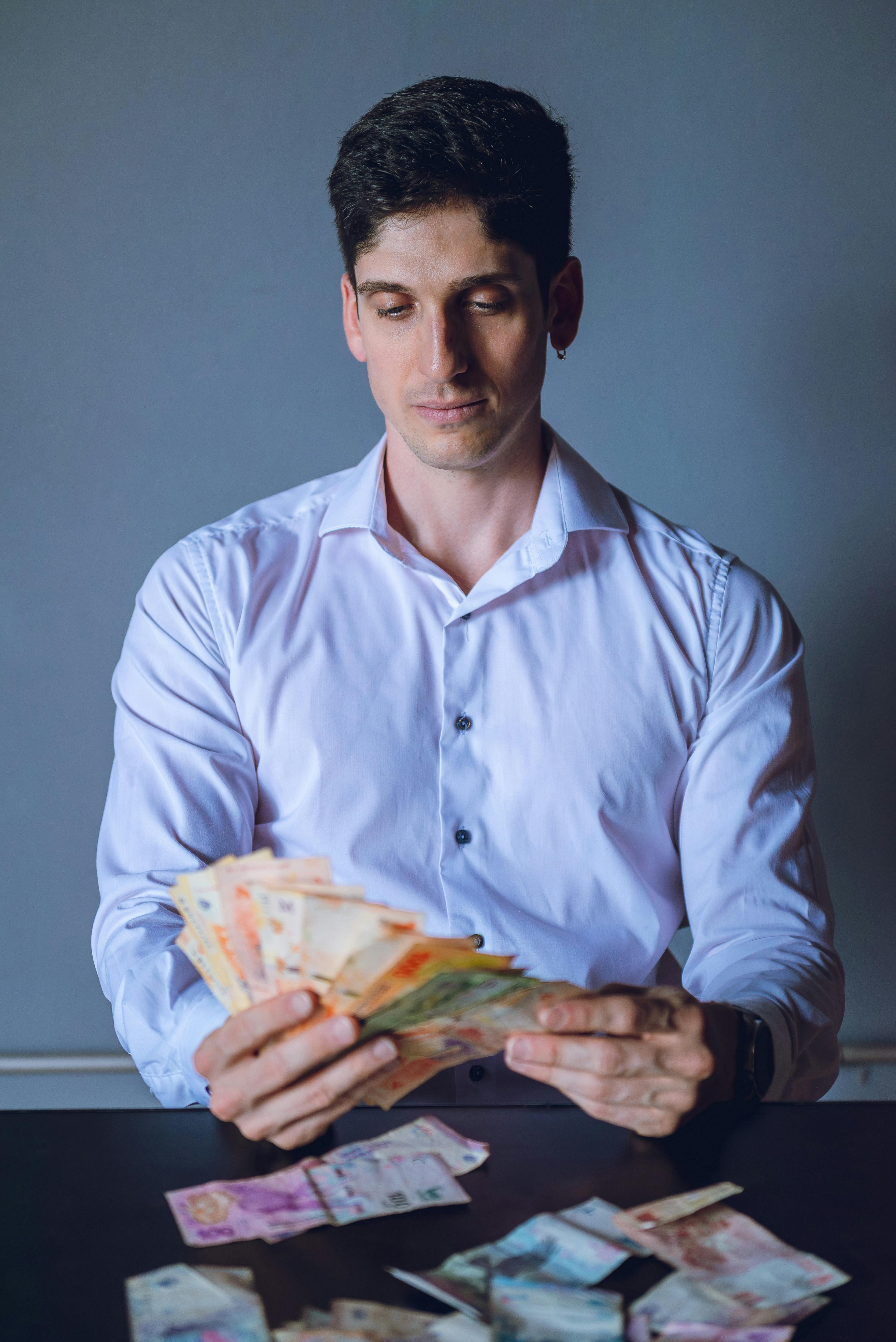 ฟรี ชายคนหนึ่งกำลังนับเงินเปโซอาร์เจนตินาอยู่ที่โต๊ะในกรุงบัวโนสไอเรส ประเทศอาร์เจนตินา โดยแสดงให้เห็นถึงสกุลเงินท้องถิ่น คลังภาพถ่าย