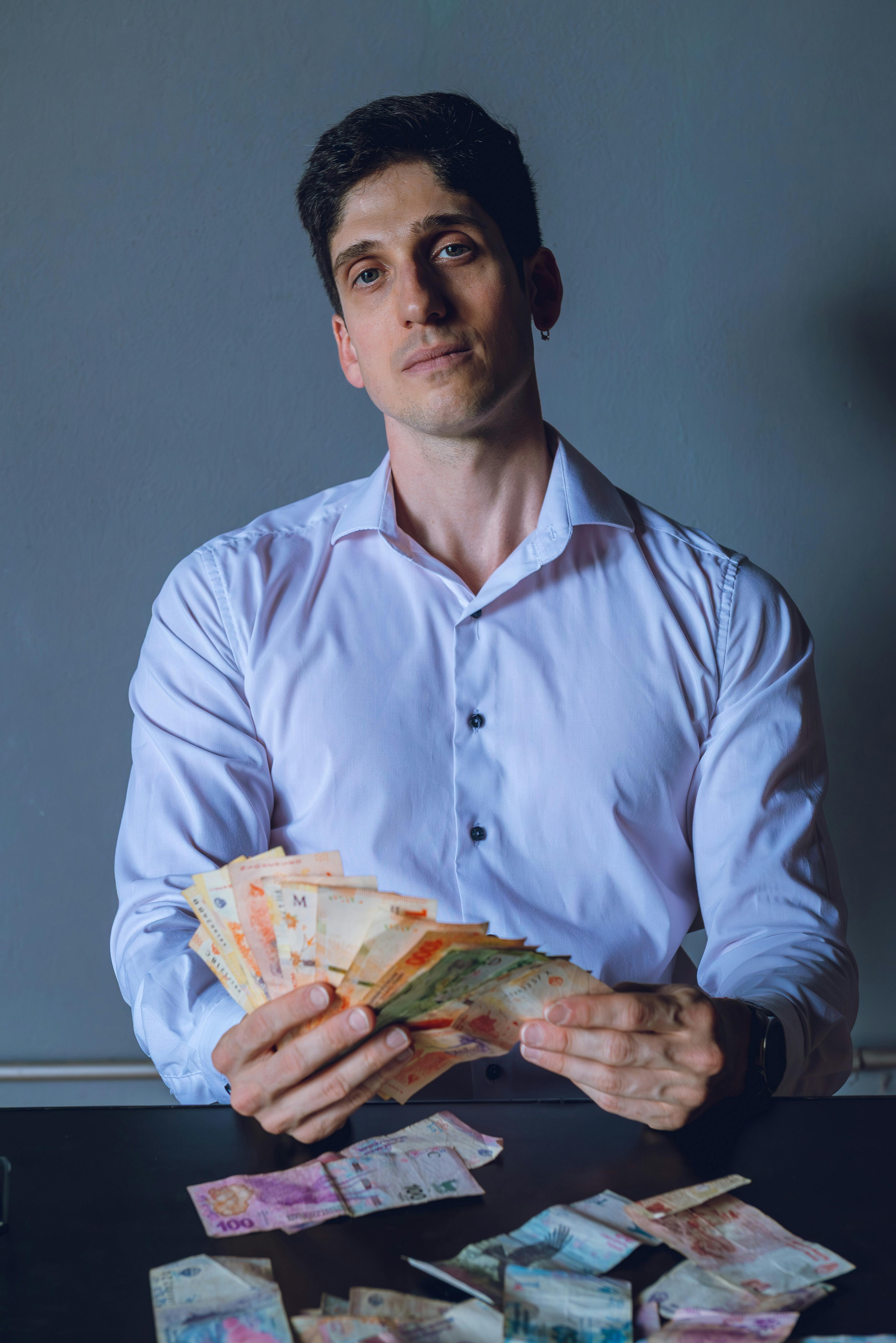 Young man in Buenos Aires counts Argentine pesos. Indoor shot with focused expression.