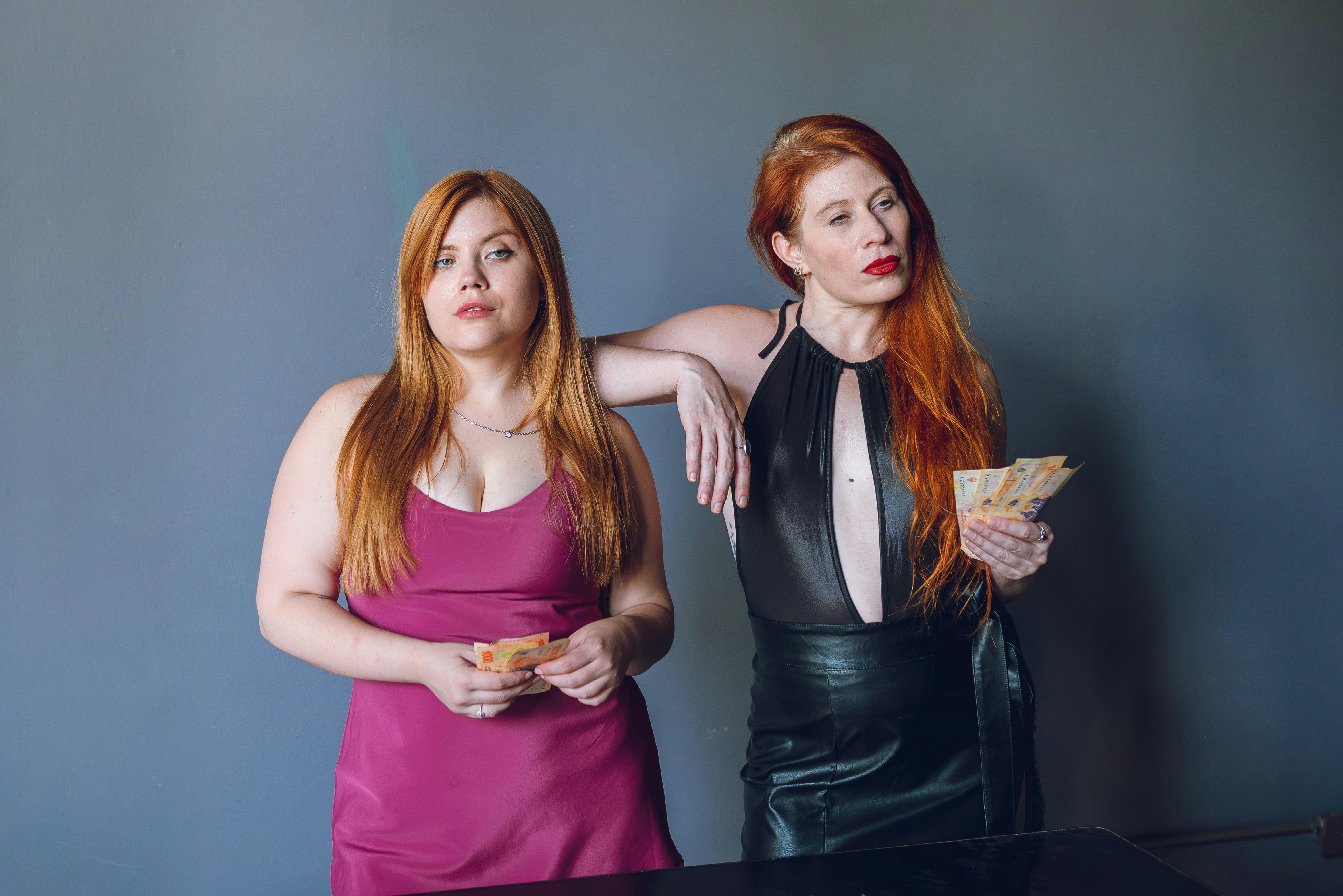 Ücretsiz Kızıl saçlı, kendinden emin iki kadın Arjantin pesosu tutuyor. Buenos Aires'te kapalı bir mekanda çekilmiş fotoğraf. Stok Fotoğraflar