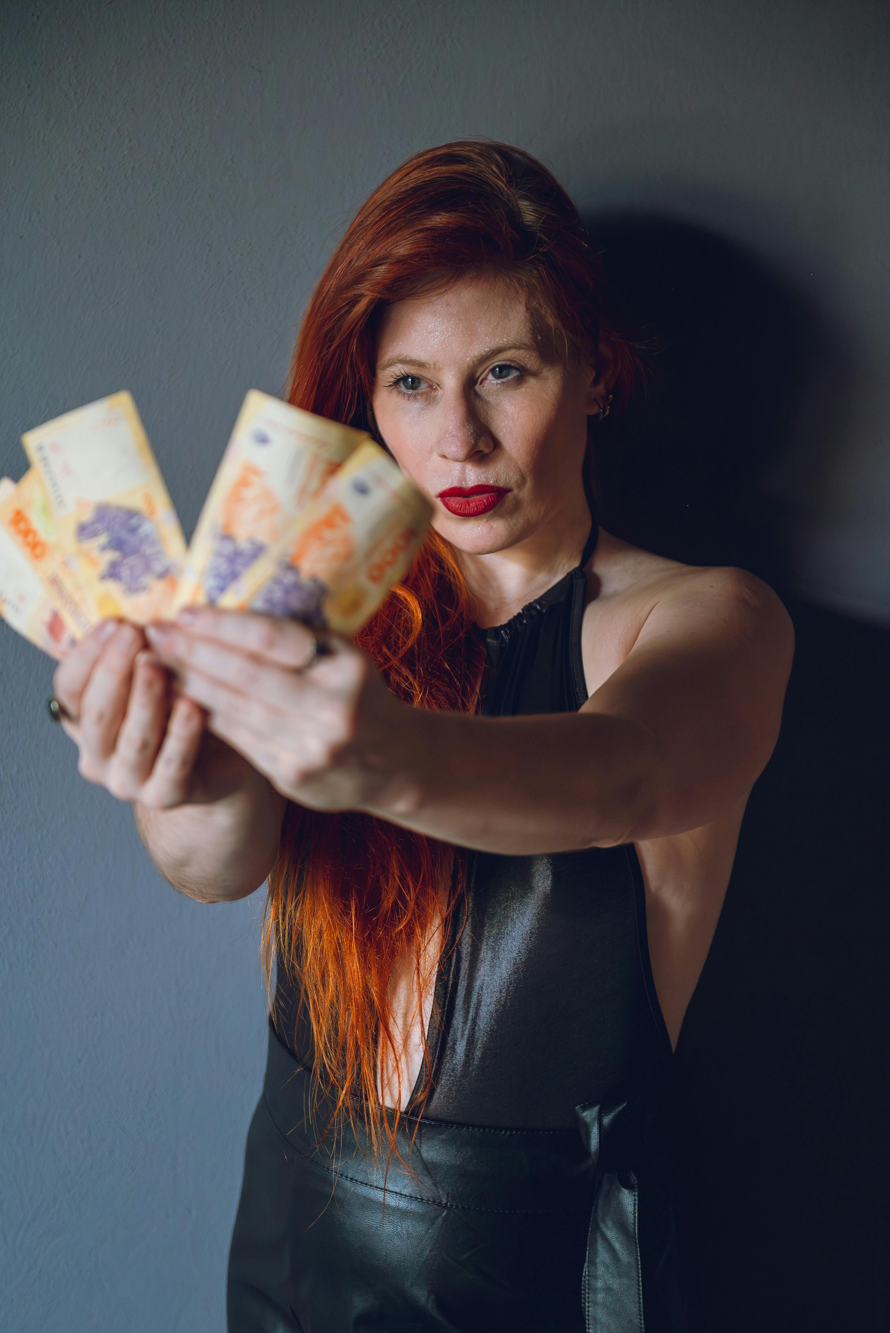 gratis Roodharige vrouw toont Argentijns geld binnenshuis, waarbij ze de link legt tussen financiën en mode. Stockfoto