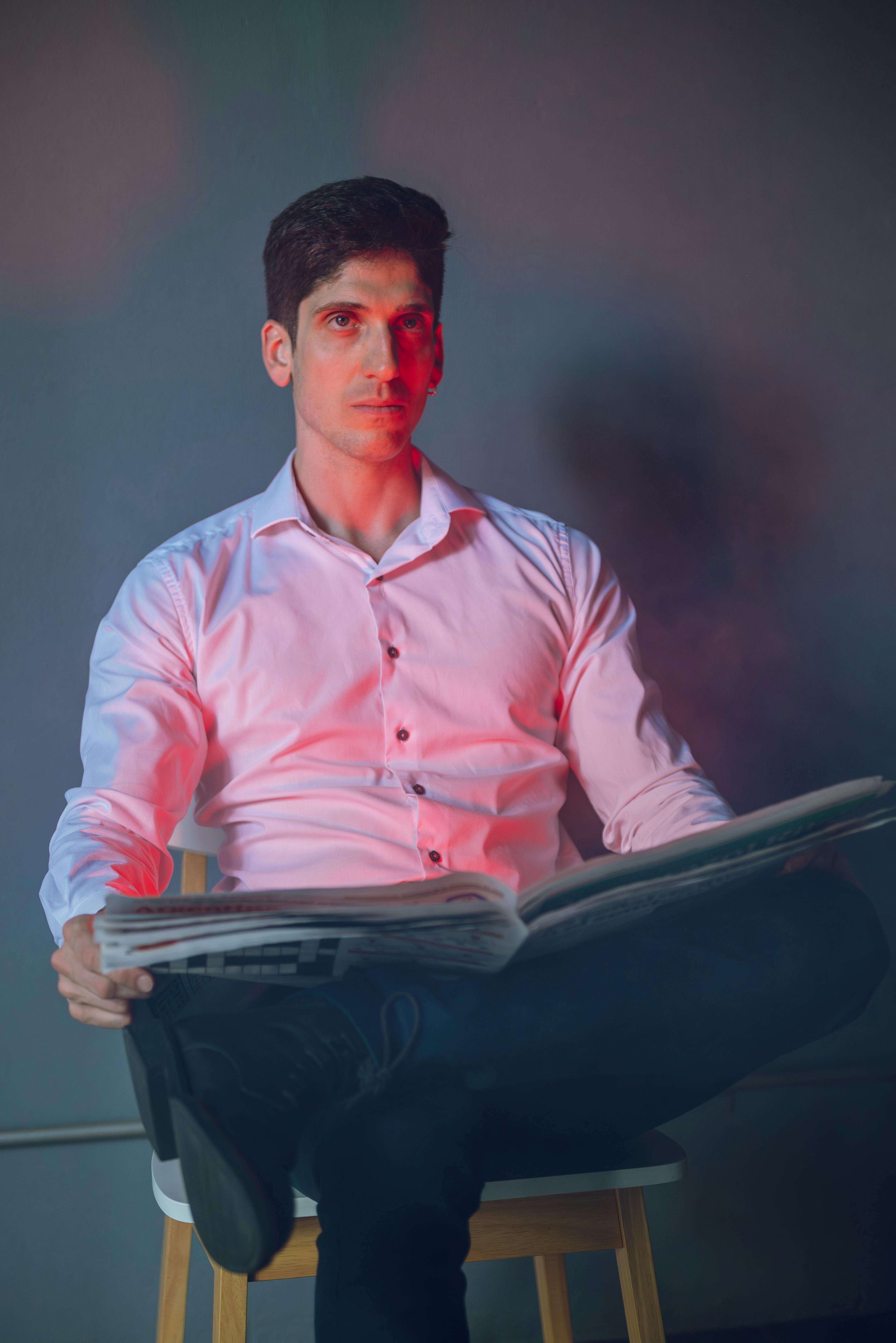 Gratis Ritratto suggestivo di un uomo seduto intento a leggere, in un'atmosfera teatrale illuminata da luci rosse e blu. Foto a disposizione