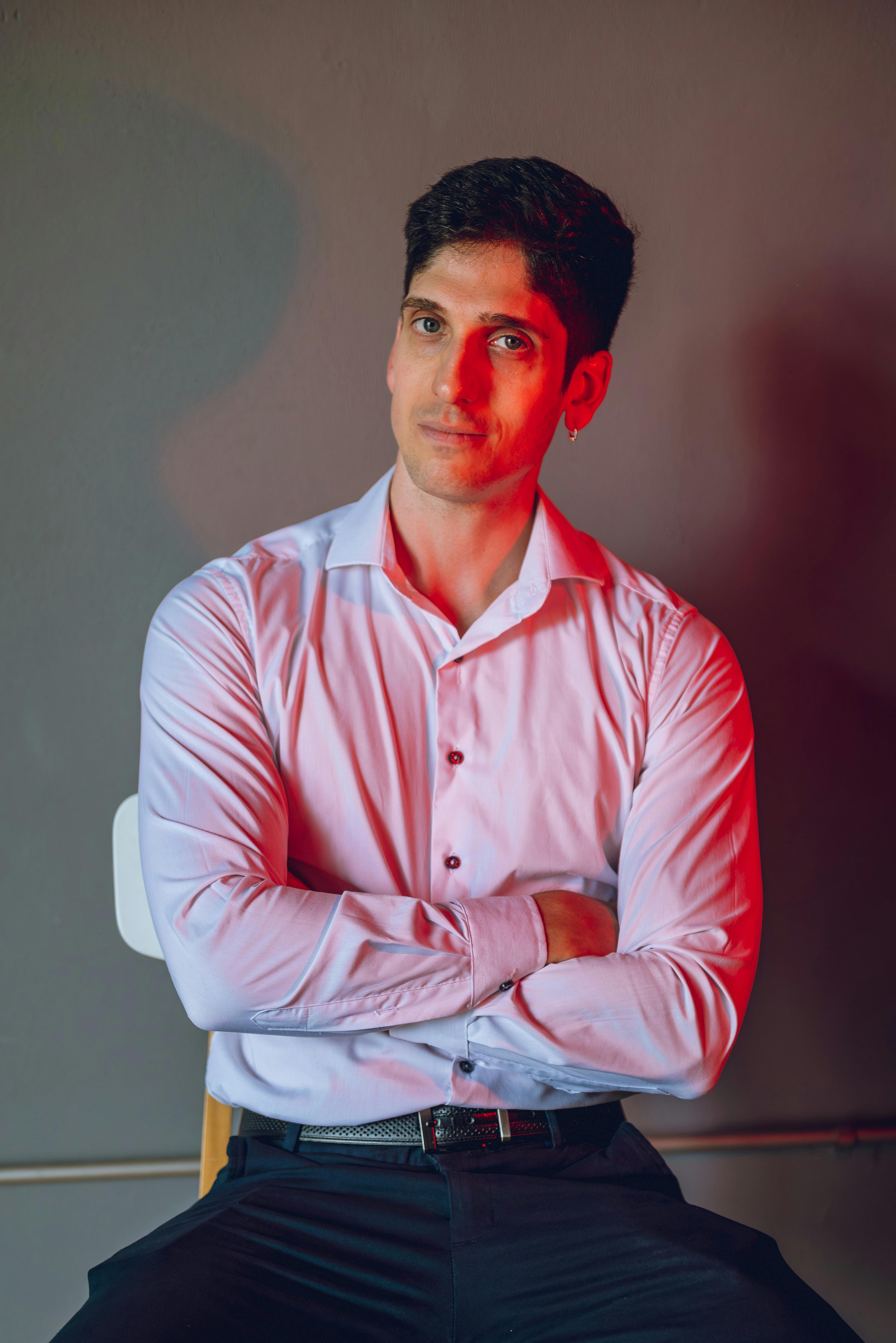 Miễn phí Chân dung một người đàn ông tự tin, ngồi trong nhà dưới ánh đèn đỏ, mặc áo sơ mi lịch sự và khoanh tay. Ảnh lưu trữ