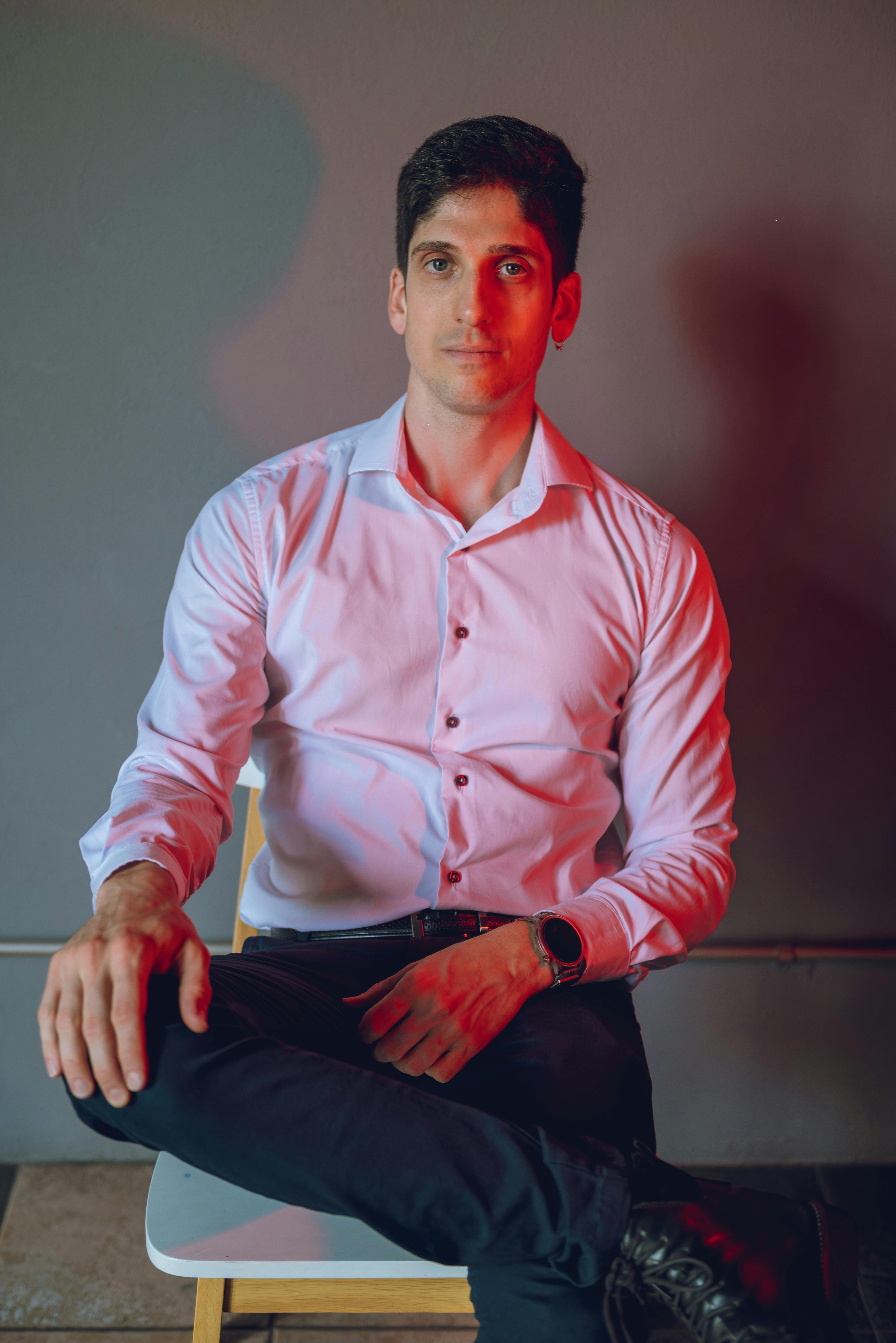 Gratis Un uomo adulto professionista seduto in un ambiente illuminato da luci artistiche, con un'espressione sicura di sé. Foto a disposizione