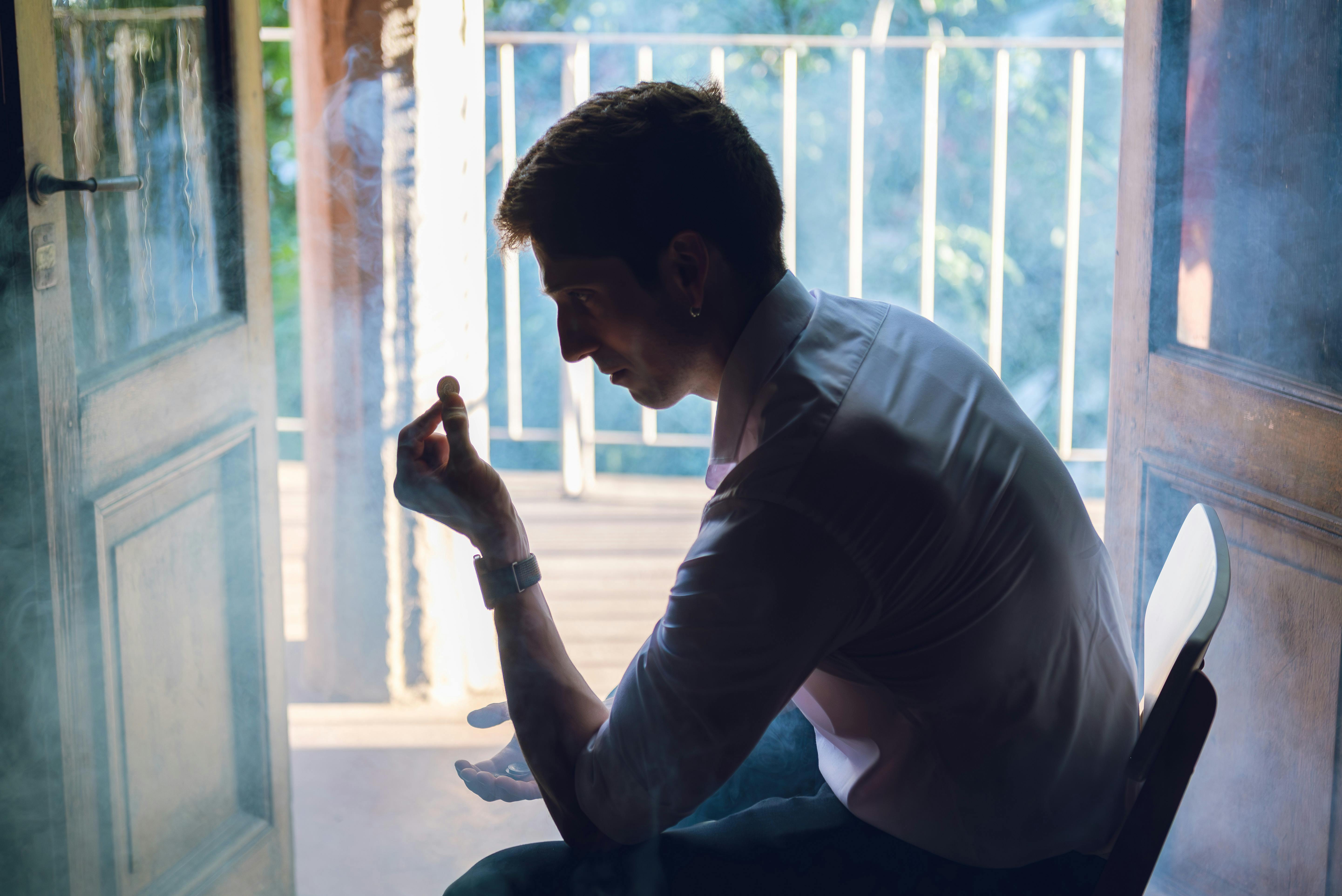 ฟรี ชายคนหนึ่งนั่งครุ่นคิดพิจารณาเหรียญอยู่ภายในอาคาร โดยมีแสงแดดส่องผ่านช่องประตูเข้ามาด้านหลัง ในกรุงบัวโนสไอเรส คลังภาพถ่าย