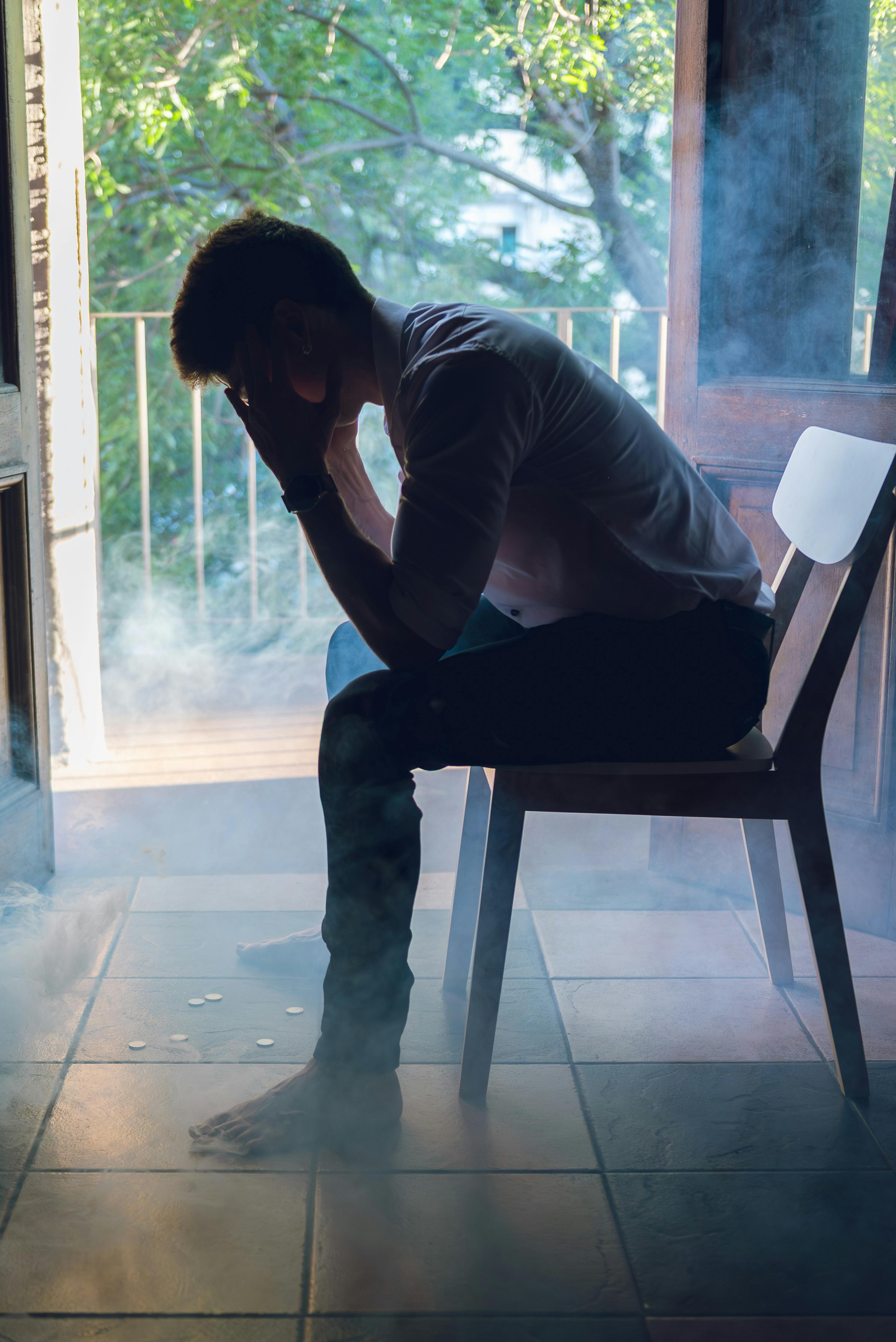 Δωρεάν Ένας άντρας κάθεται σε βαθιές σκέψεις σε μια καρέκλα μέσα σε καπνό, σε εσωτερικό χώρο στο Μπουένος Άιρες της Αργεντινής. Φωτογραφία από στοκ φωτογραφιών