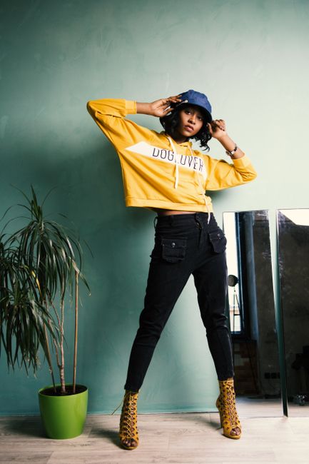 A fashionable woman poses indoors in a trendy yellow hoodie and jeans.