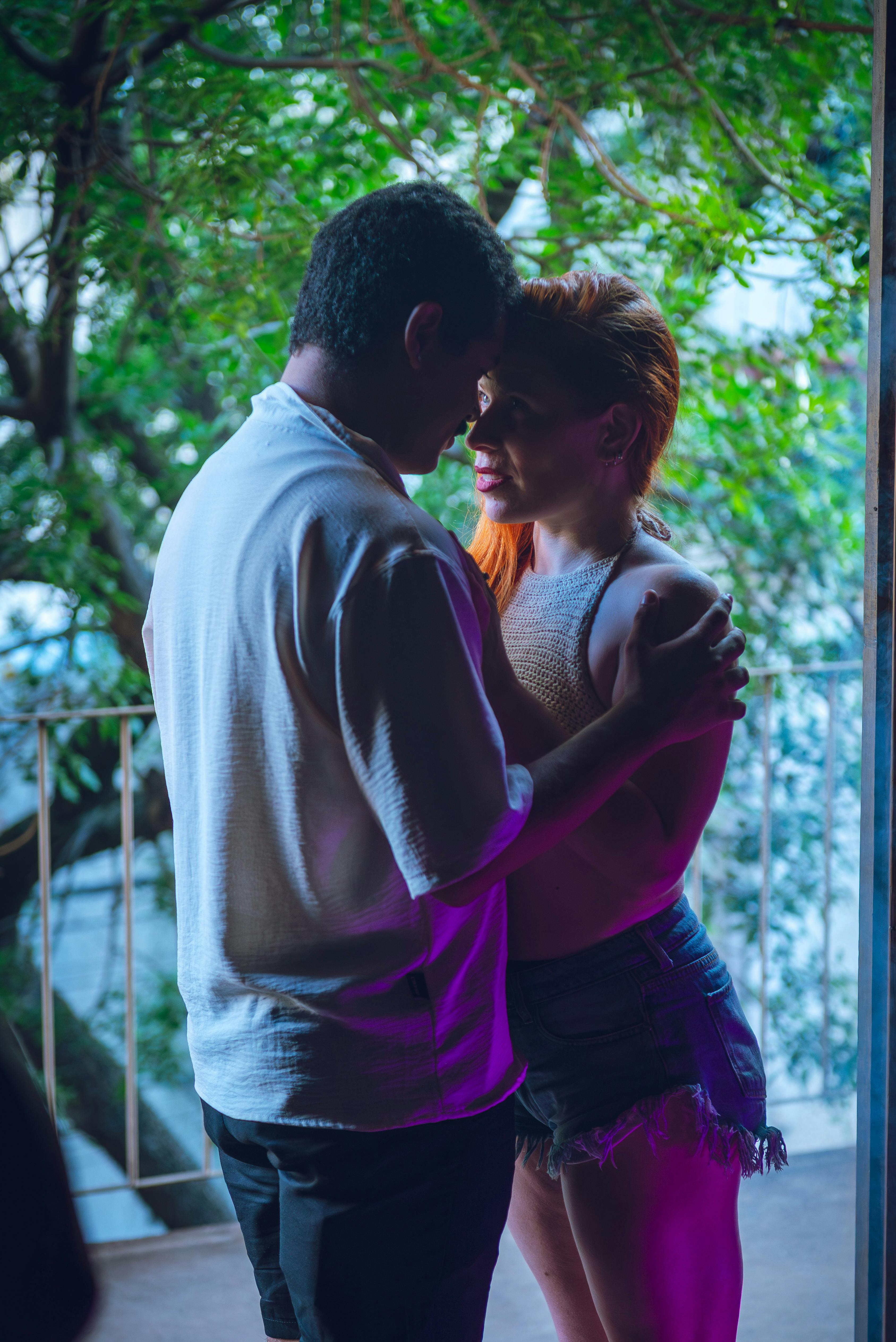 Ücretsiz Arka planda ağaçların bulunduğu bir balkonda kucaklaşan bir çiftin samimi anı. Stok Fotoğraflar