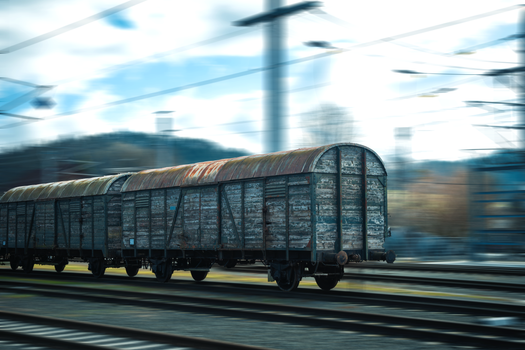 Rustic cargo train moving fast across railway tracks, blurred motion effect.