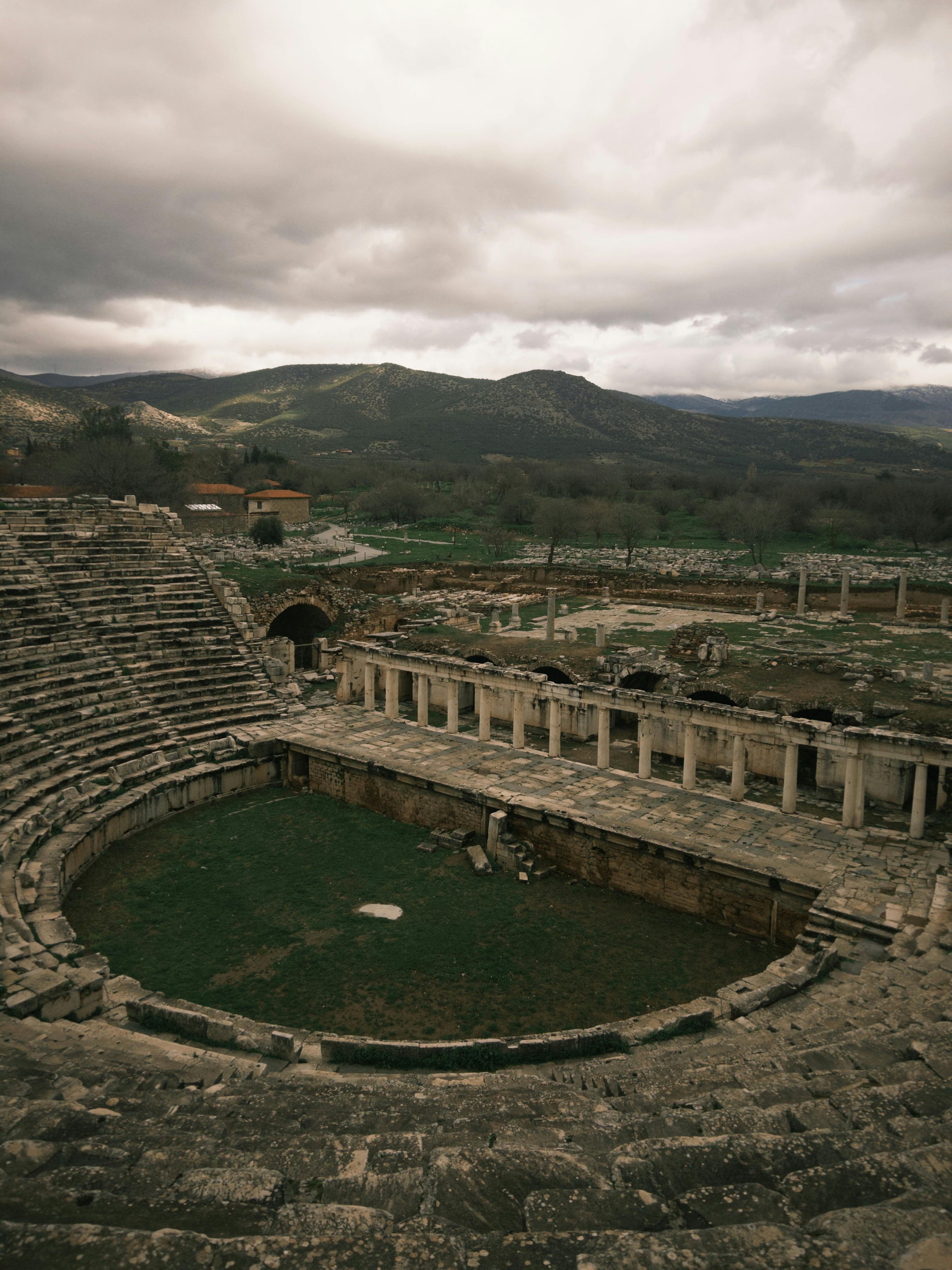 Gratuit Vue imprenable sur les ruines d'un ancien théâtre à Aydın, en Turquie, entourées de collines sous un ciel nuageux spectaculaire. Photos