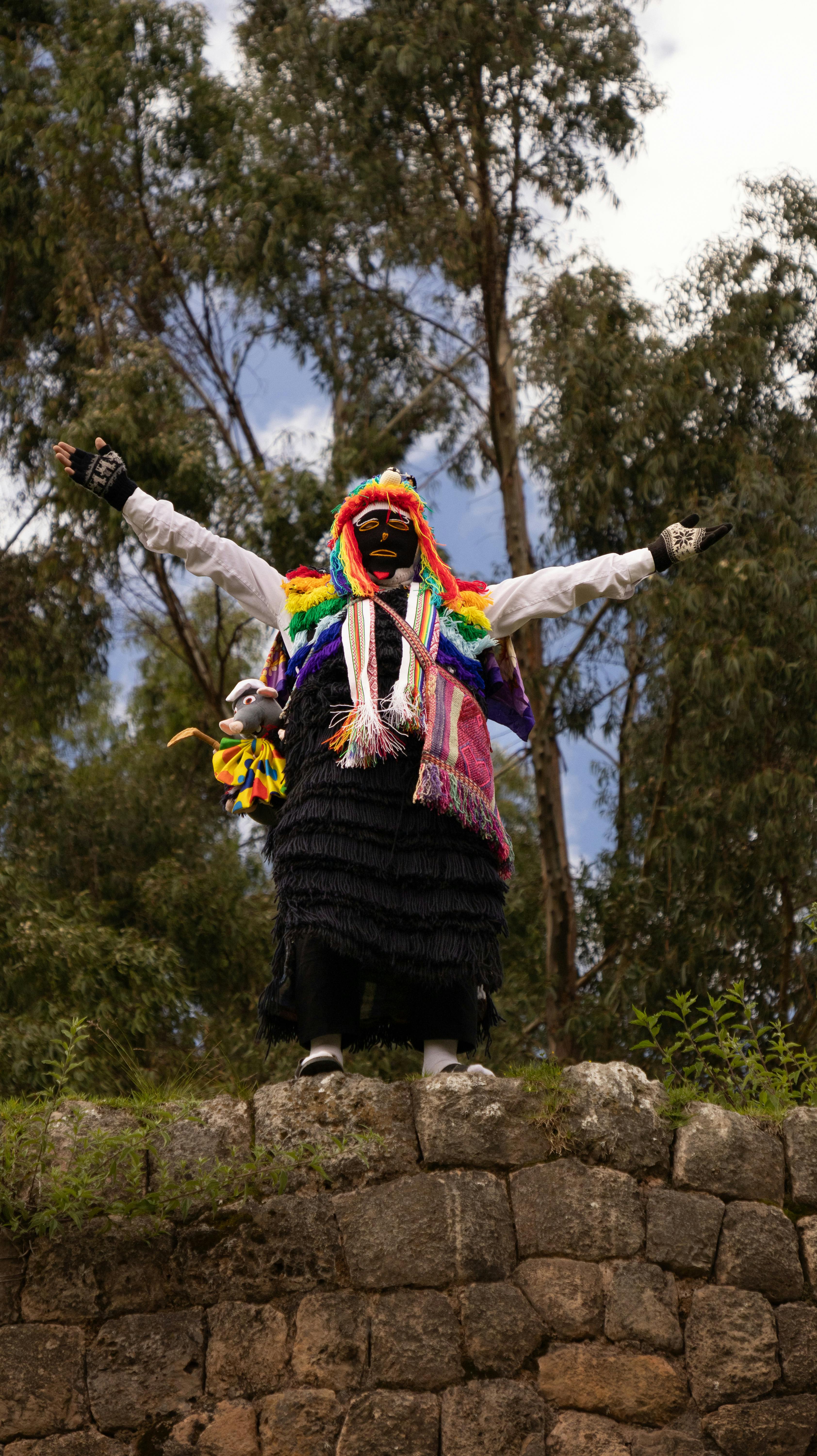 Person in colorful traditional attire stands on stone structure outdoors.