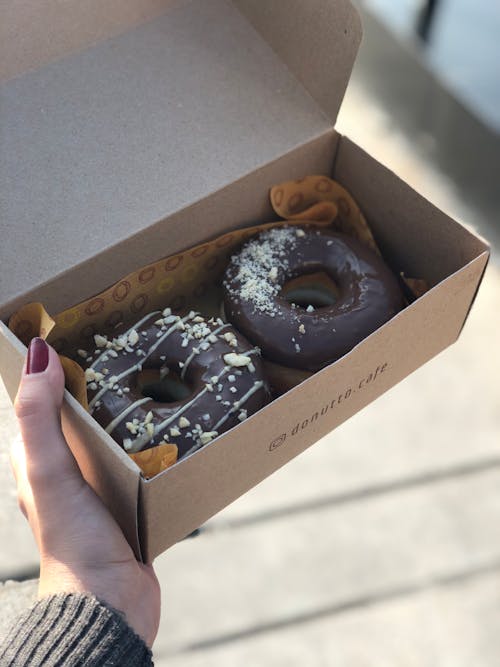 Woman Holding A Brown Cardboard Box With Chocolate Doughnuts