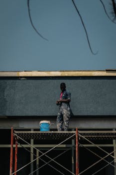 A construction worker standing on scaffolding with a clear blue sky behind, showcasing construction themes.