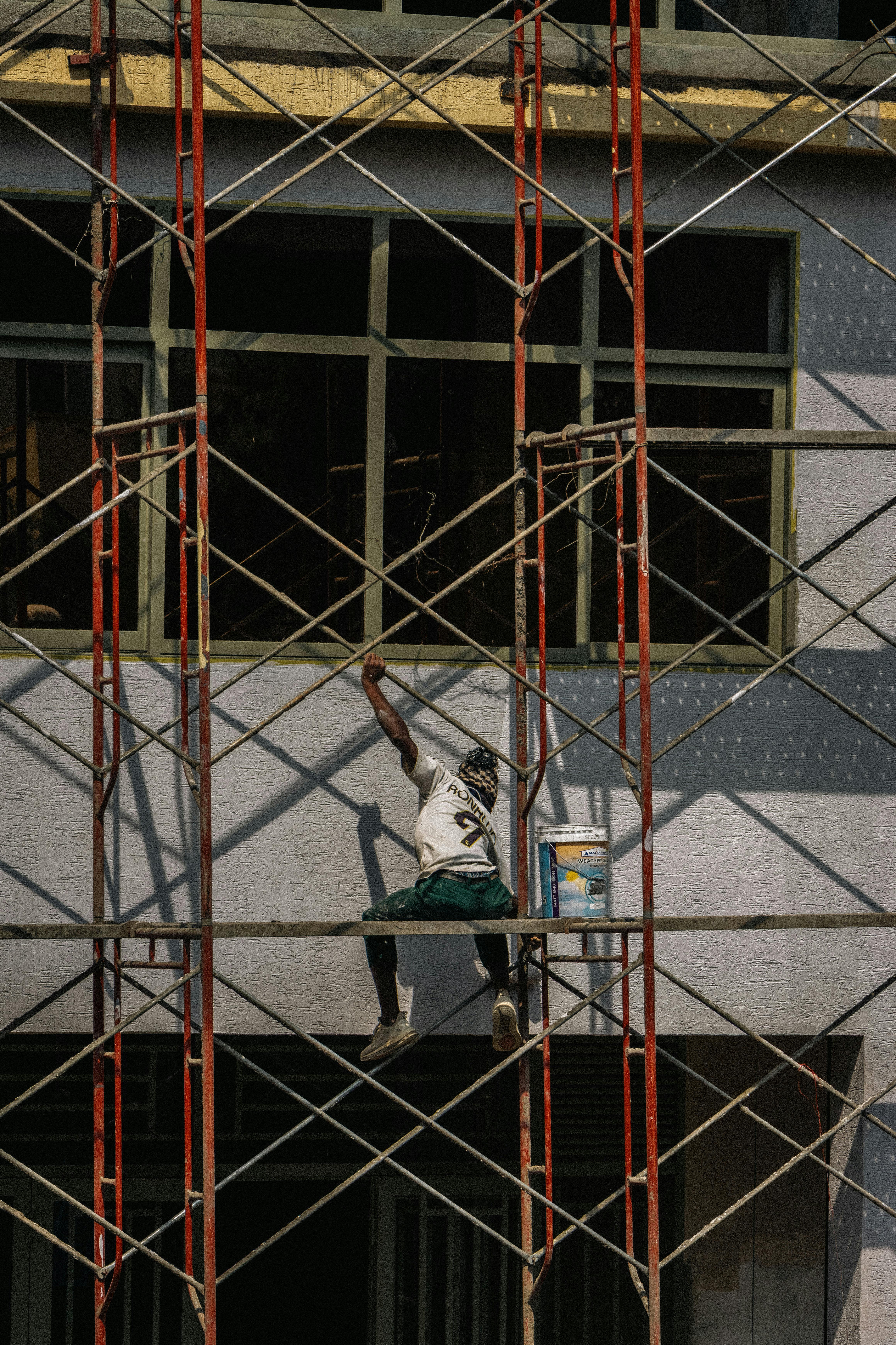 Gratuit Un muncitor în construcții vopsește fațada unei clădiri în timp ce se echilibrează pe o schelă. Fotografie de stoc