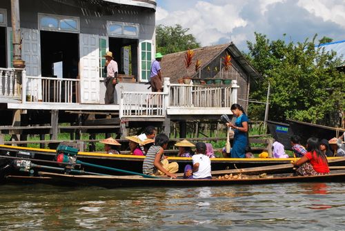 Free Colorful scene of a floating market with boats and people by a stilt house in Southeast Asia. Stock Photo