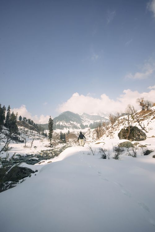 Free A serene winter scene in Pahalgam featuring a horse rider amidst snow-covered mountains. Stock Photo