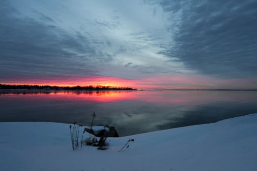 Breathtaking winter sunset reflecting on a calm lake, surrounded by snow.