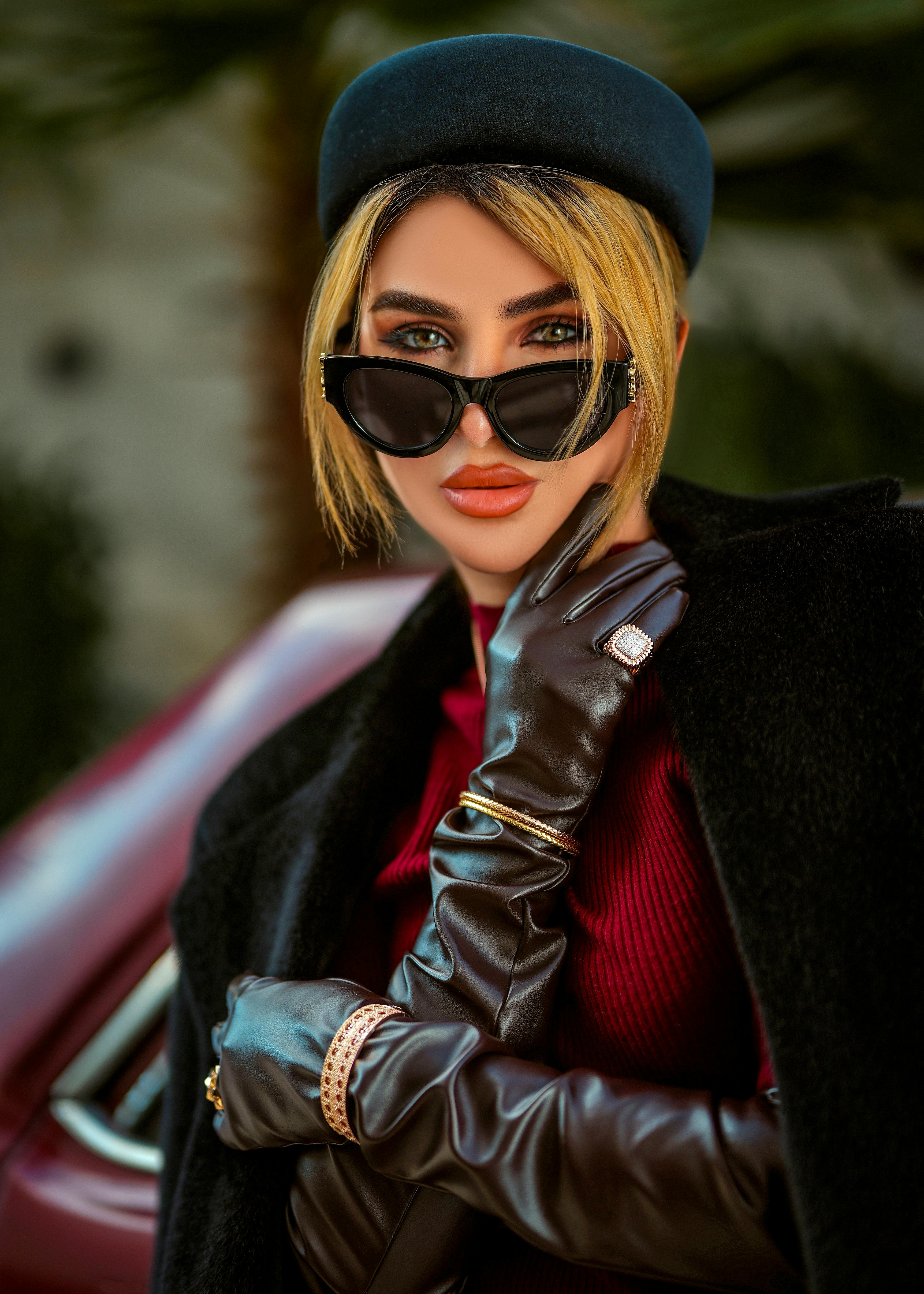 Miễn phí Người phụ nữ sành điệu đeo kính râm và găng tay tạo dáng tự tin với phông nền ngoài trời mờ ảo. Ảnh lưu trữ