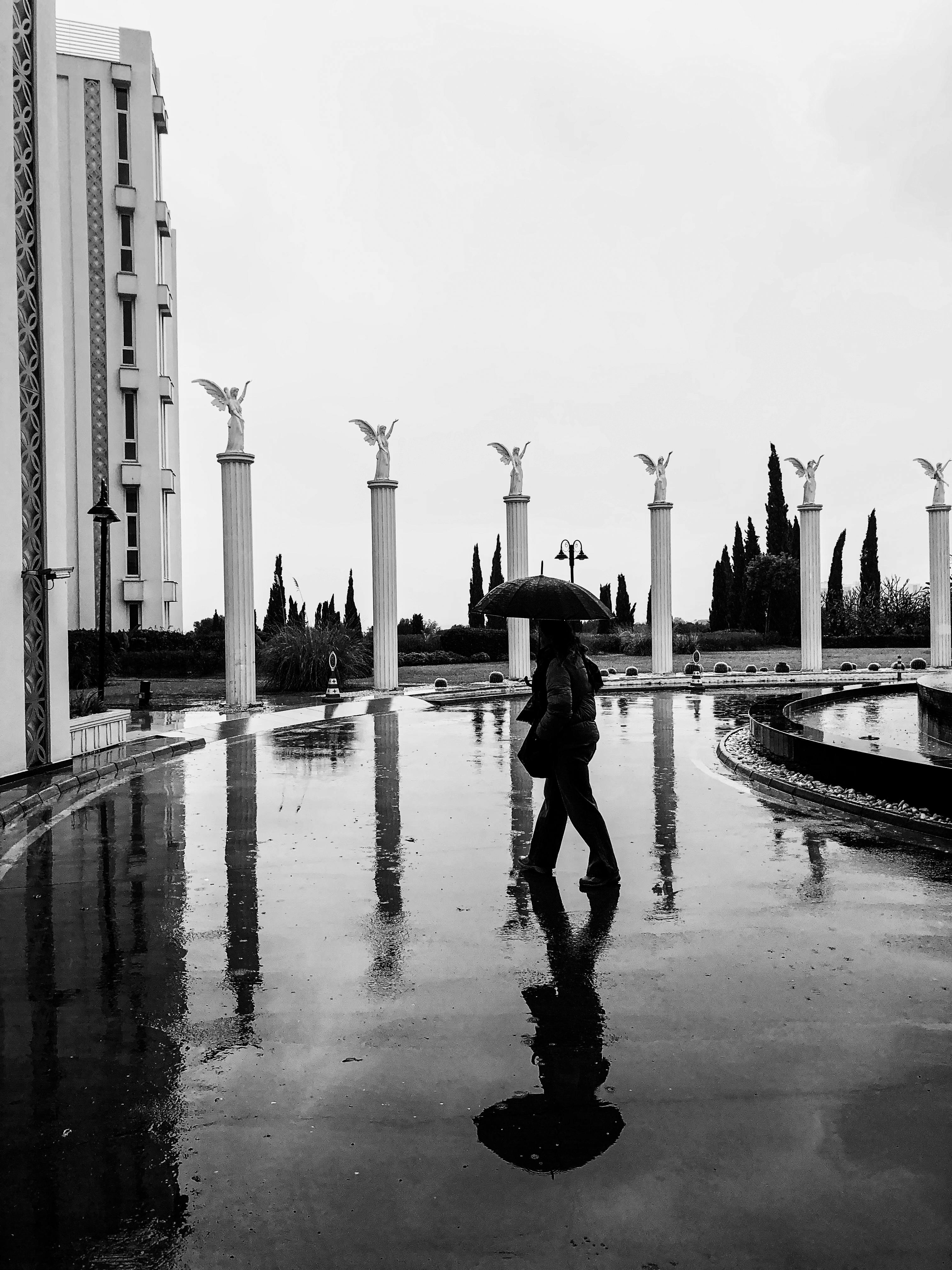 Ücretsiz Islak ve yansıtıcı bir şehir manzarası içinde şemsiyeli yalnız bir kişiyi gösteren tek renkli bir sahne. Stok Fotoğraflar