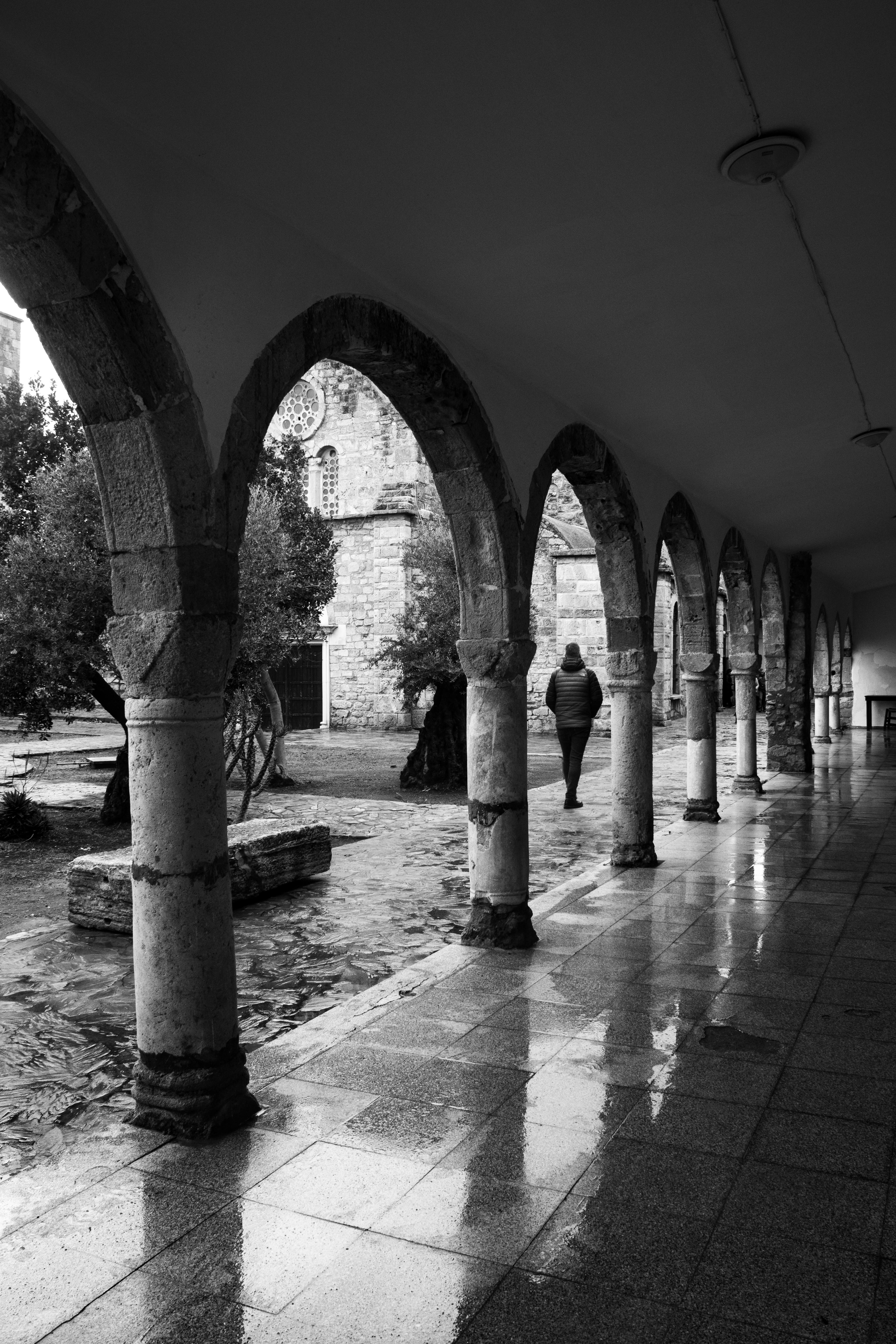 Ücretsiz Kemerli tarihi bir taş manastırın içinden yürüyen bir kişinin siyah beyaz fotoğrafı. Stok Fotoğraflar