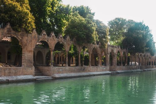 Free Scenic view of ancient stone archways by a tranquil river under lush green trees. Stock Photo