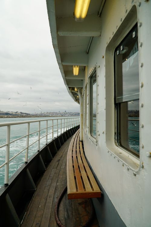 Free A ferry deck with a curved railing, city view, and cloudy sky. Stock Photo